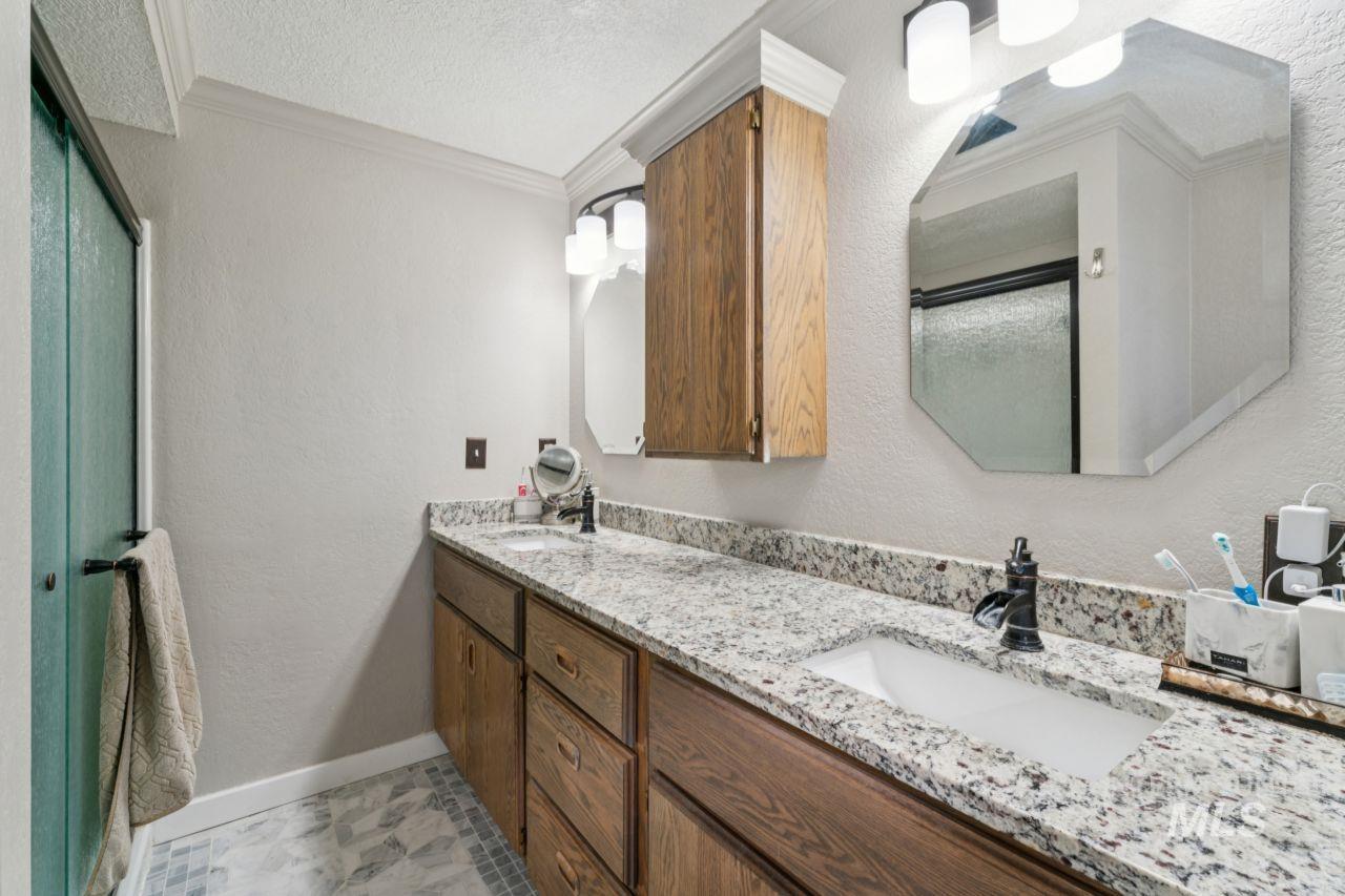 Full bath with a textured wall, ornamental molding, a stall shower, a textured ceiling, and double vanity