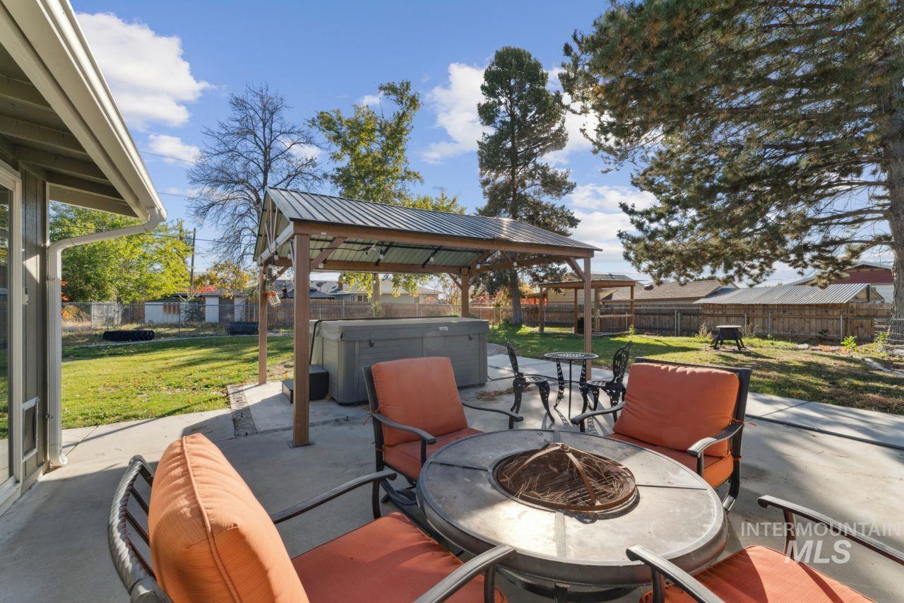 Fenced backyard with a patio area, a hot tub, a fire pit, and a gazebo