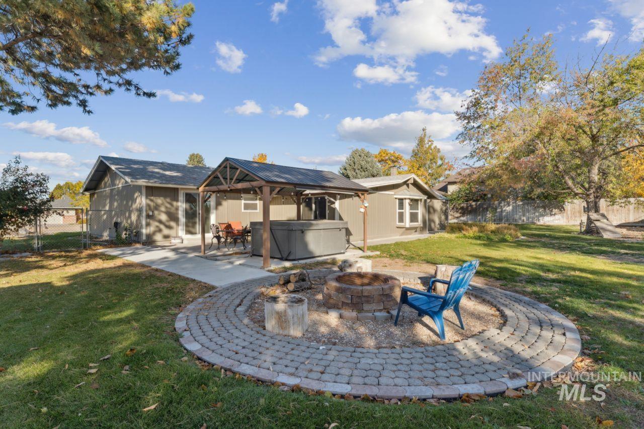 Rear view of property with a hot tub, a patio area, a fenced backyard, and an outdoor fire pit
