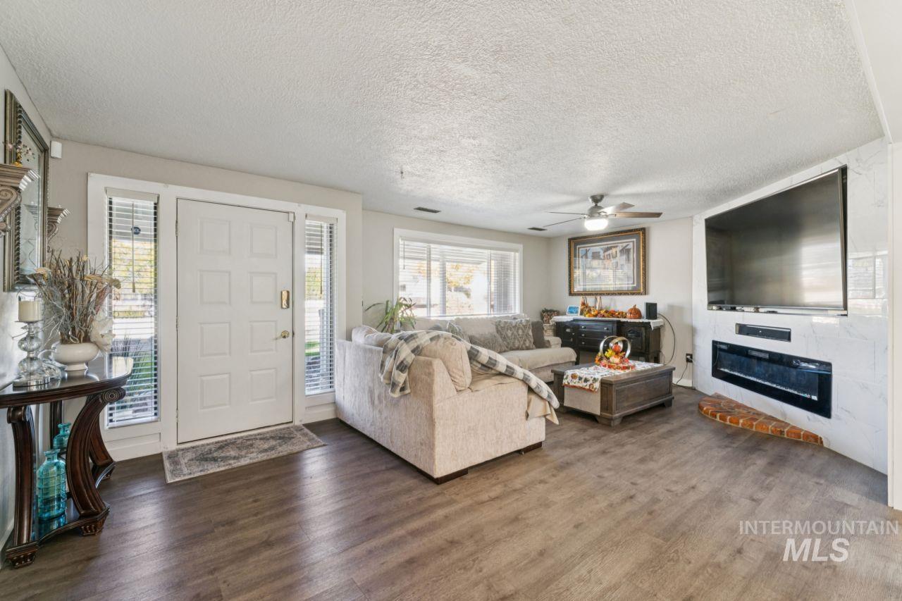 Living area featuring a textured ceiling, dark wood-style floors, a ceiling fan, and a glass covered fireplace