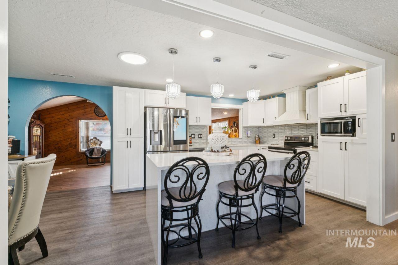 Kitchen featuring a breakfast bar area, a textured ceiling, pendant lighting, arched walkways, and white cabinets