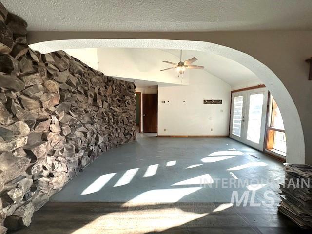 Unfurnished living room with arched walkways, french doors, a ceiling fan, a textured ceiling, and vaulted ceiling