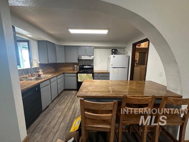 Kitchen featuring gray cabinets, a textured wall, black appliances, tasteful backsplash, and dark wood finished floors