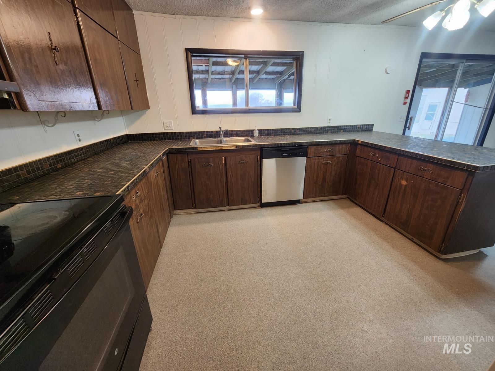 Kitchen with dark countertops, dark brown cabinetry, black range with electric stovetop, a textured ceiling, and dishwasher