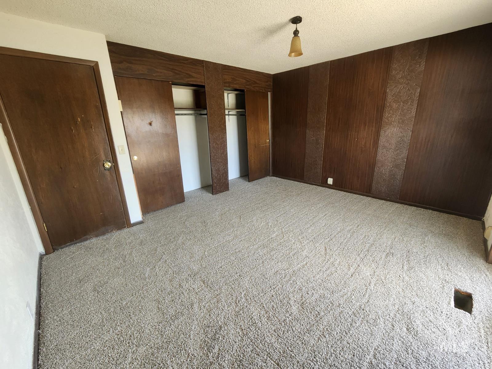 Unfurnished bedroom with a textured ceiling, light colored carpet, two closets, and wooden walls