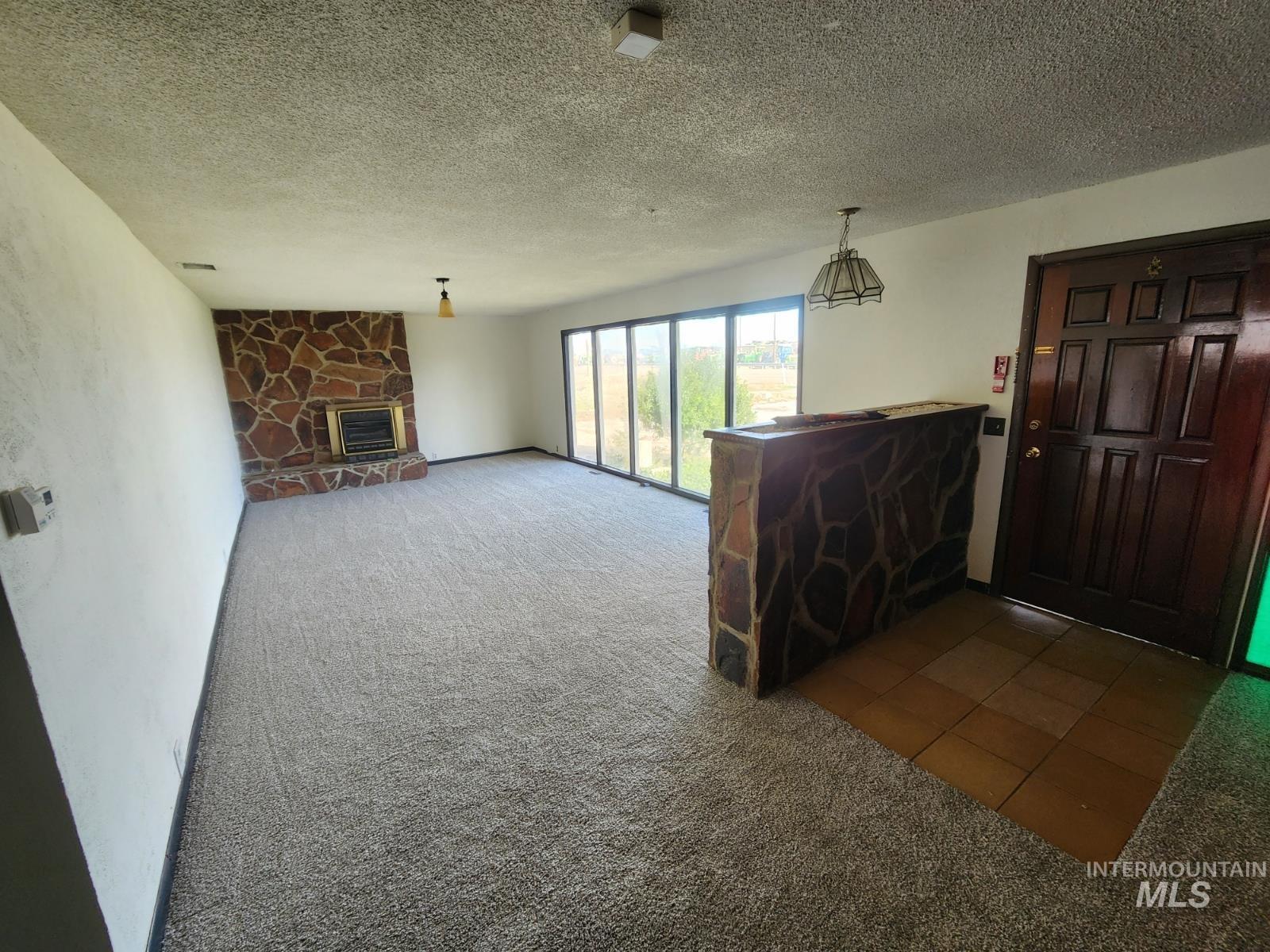 Unfurnished living room featuring carpet, a stone fireplace, a textured ceiling, and tile patterned floors