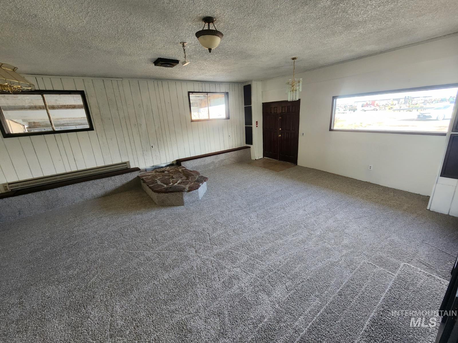 Carpeted empty room with wooden walls, a baseboard radiator, and a textured ceiling