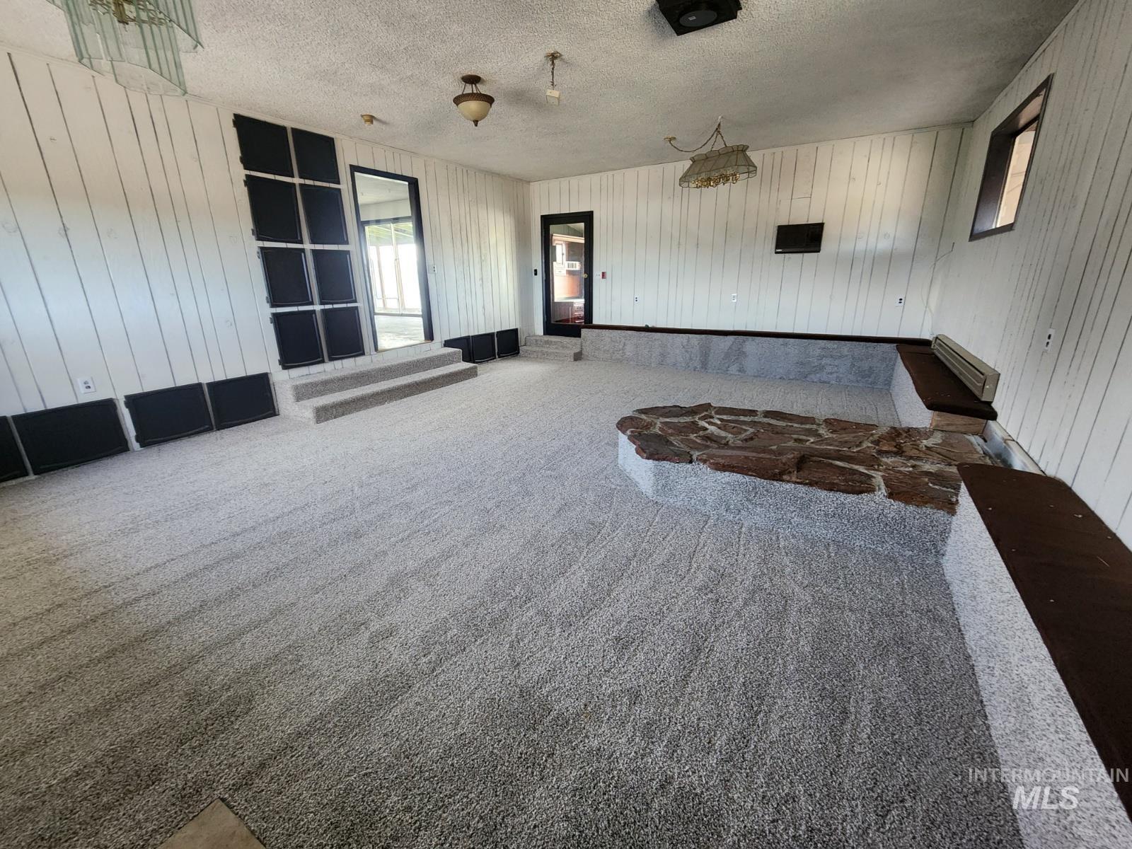 Spare room featuring a textured ceiling, wooden walls, carpet floors, and baseboard heating
