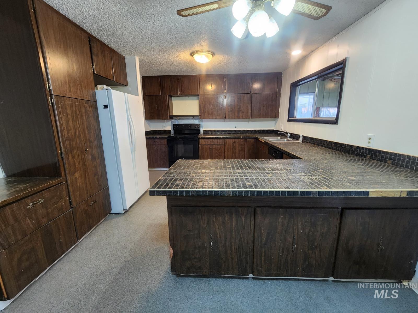 Kitchen with dark brown cabinets, freestanding refrigerator, black / electric stove, a textured ceiling, and ceiling fan