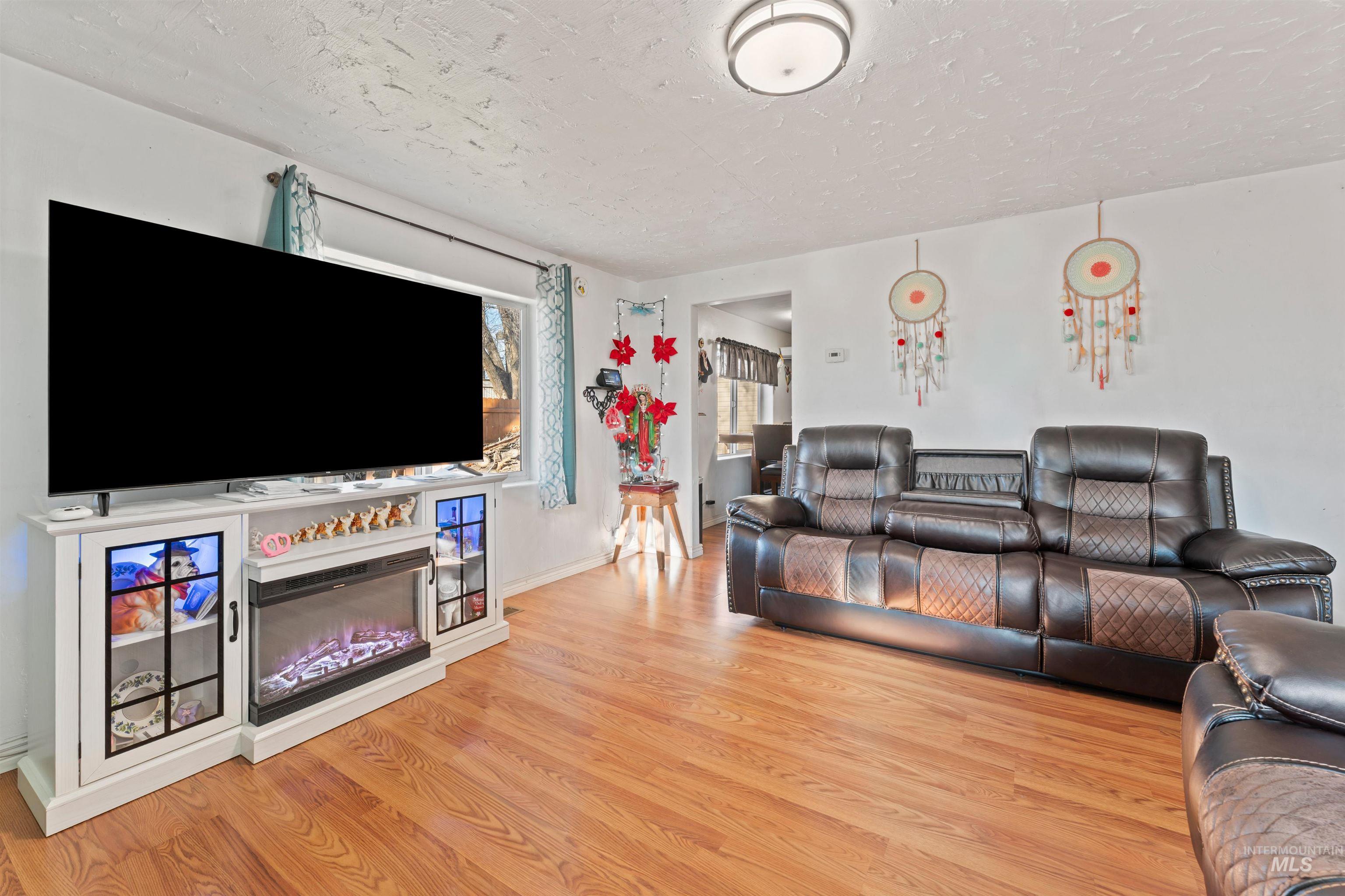 Living area featuring wood finished floors, a textured ceiling, and a glass covered fireplace