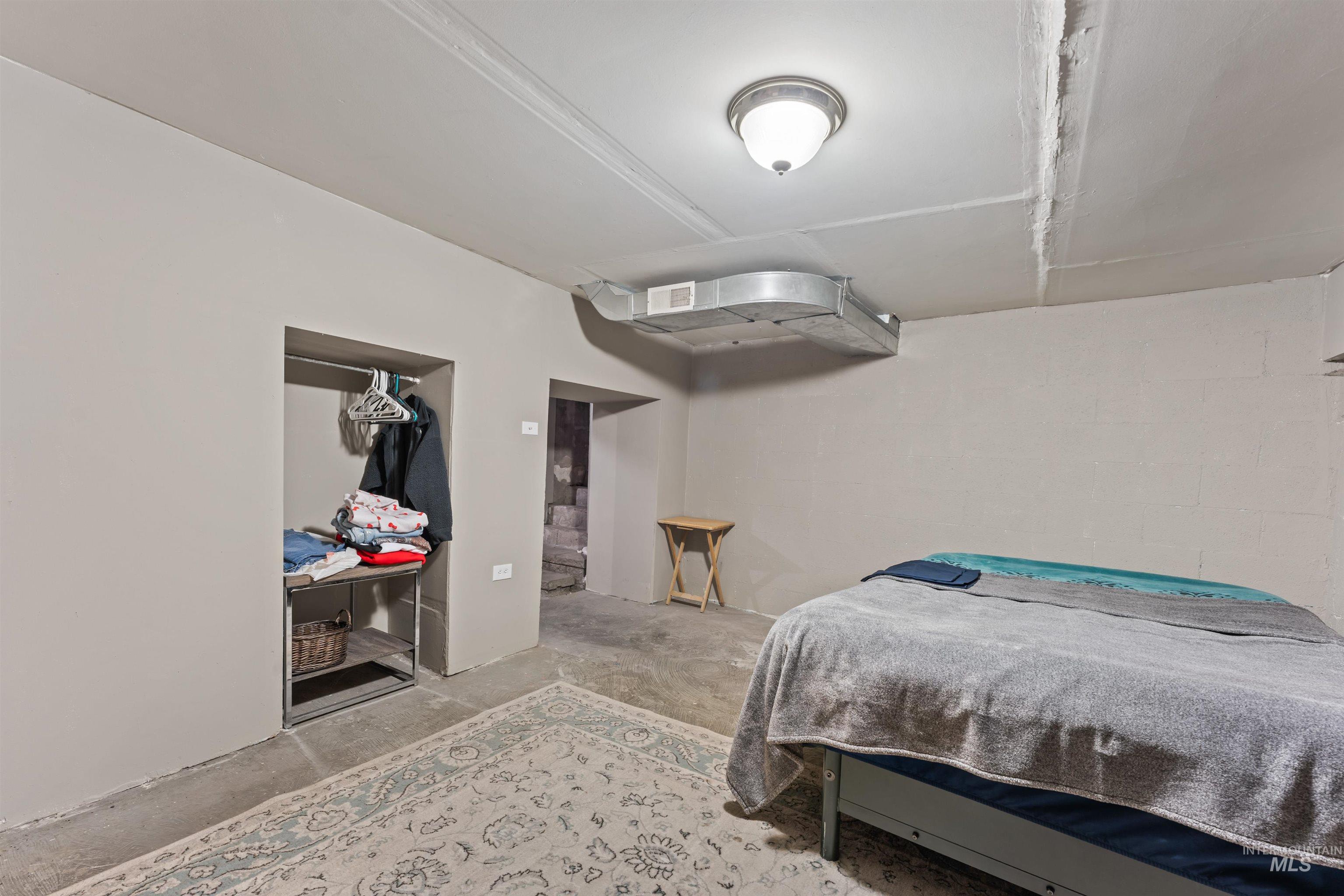 Bedroom featuring concrete block wall, a closet, and unfinished concrete flooring