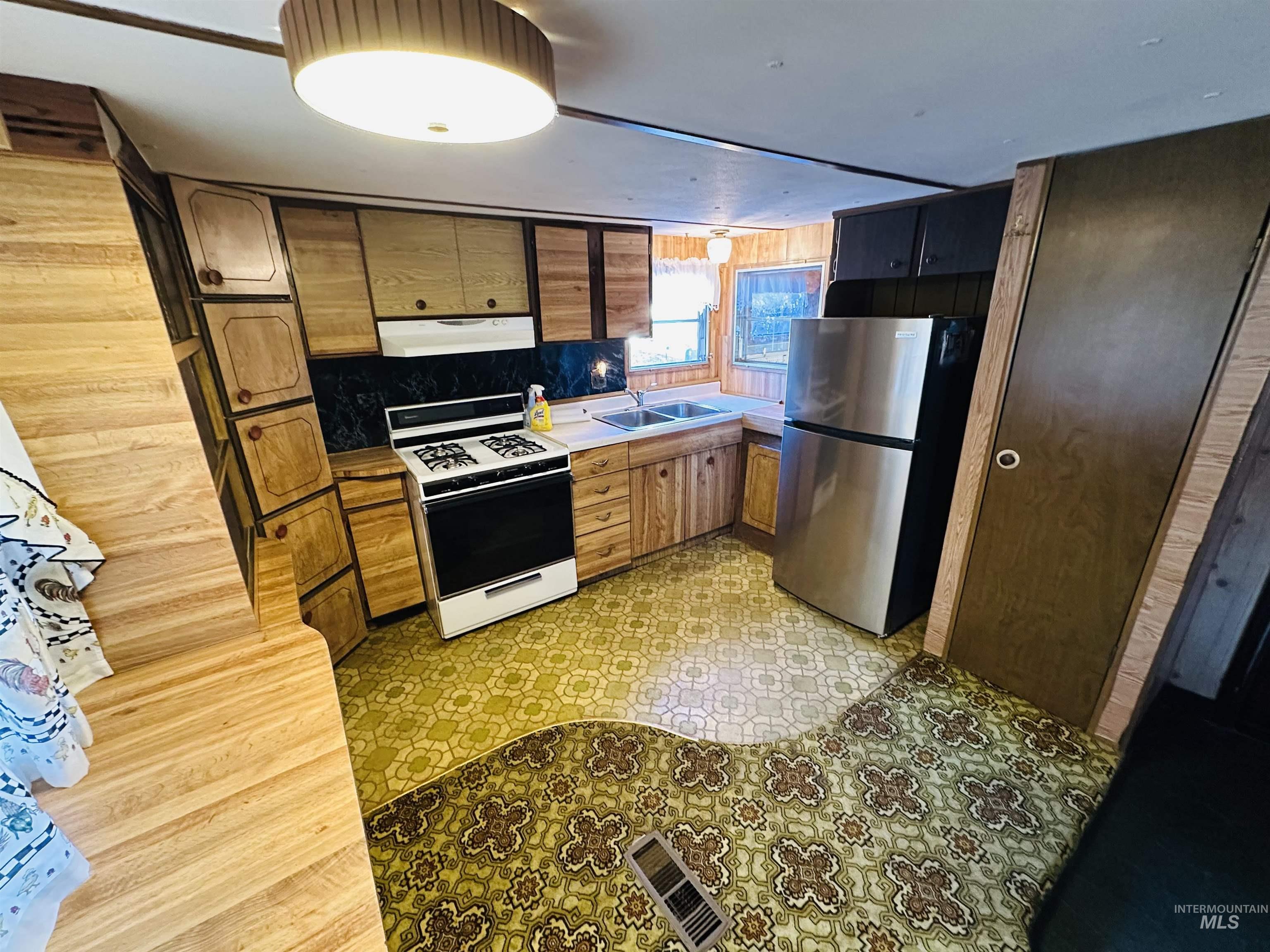 Kitchen with light floors, white range with gas stovetop, freestanding refrigerator, under cabinet range hood, and light countertops