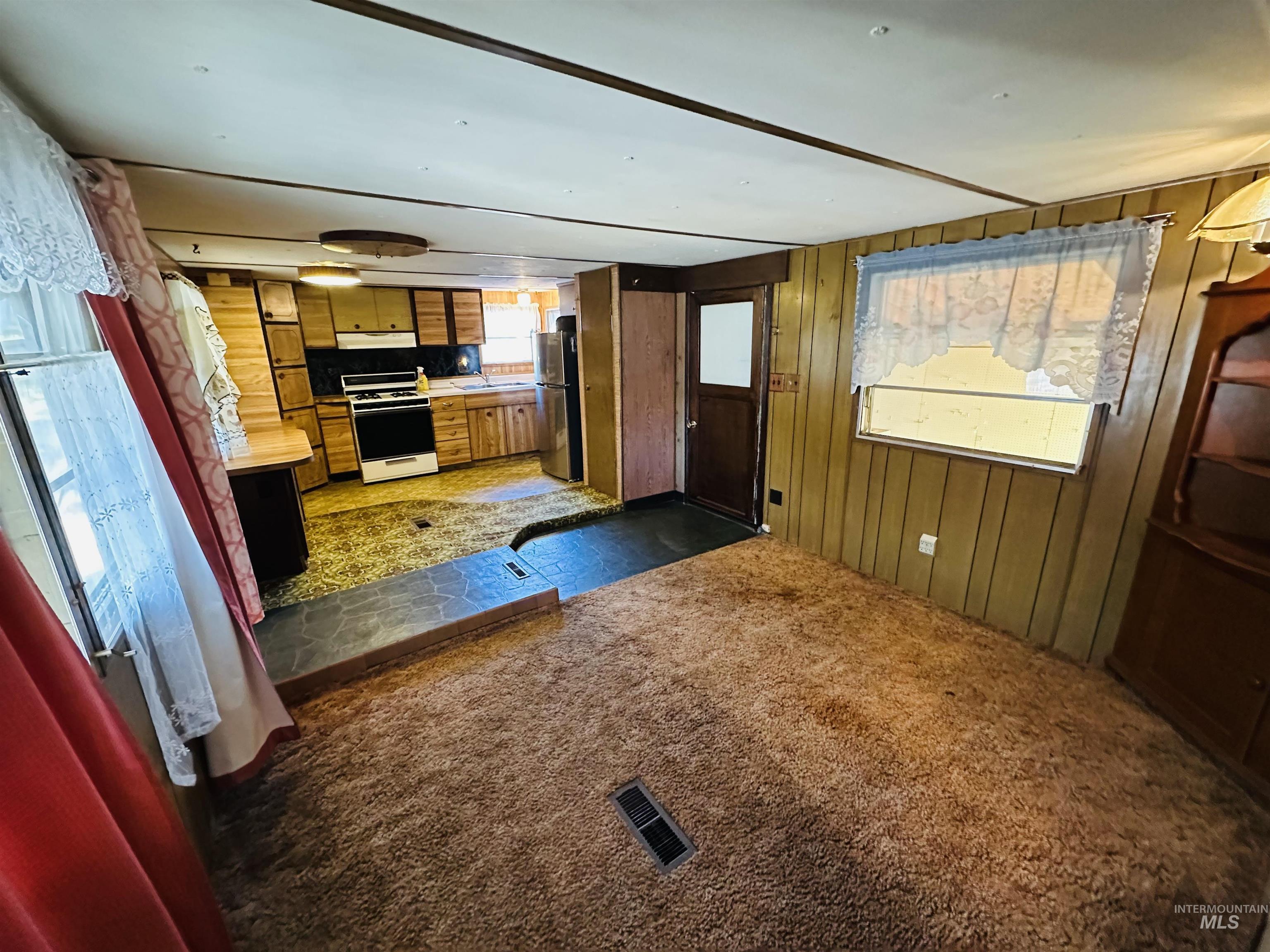 Kitchen featuring wood walls, brown cabinets, white range with gas cooktop, dark carpet, and freestanding refrigerator