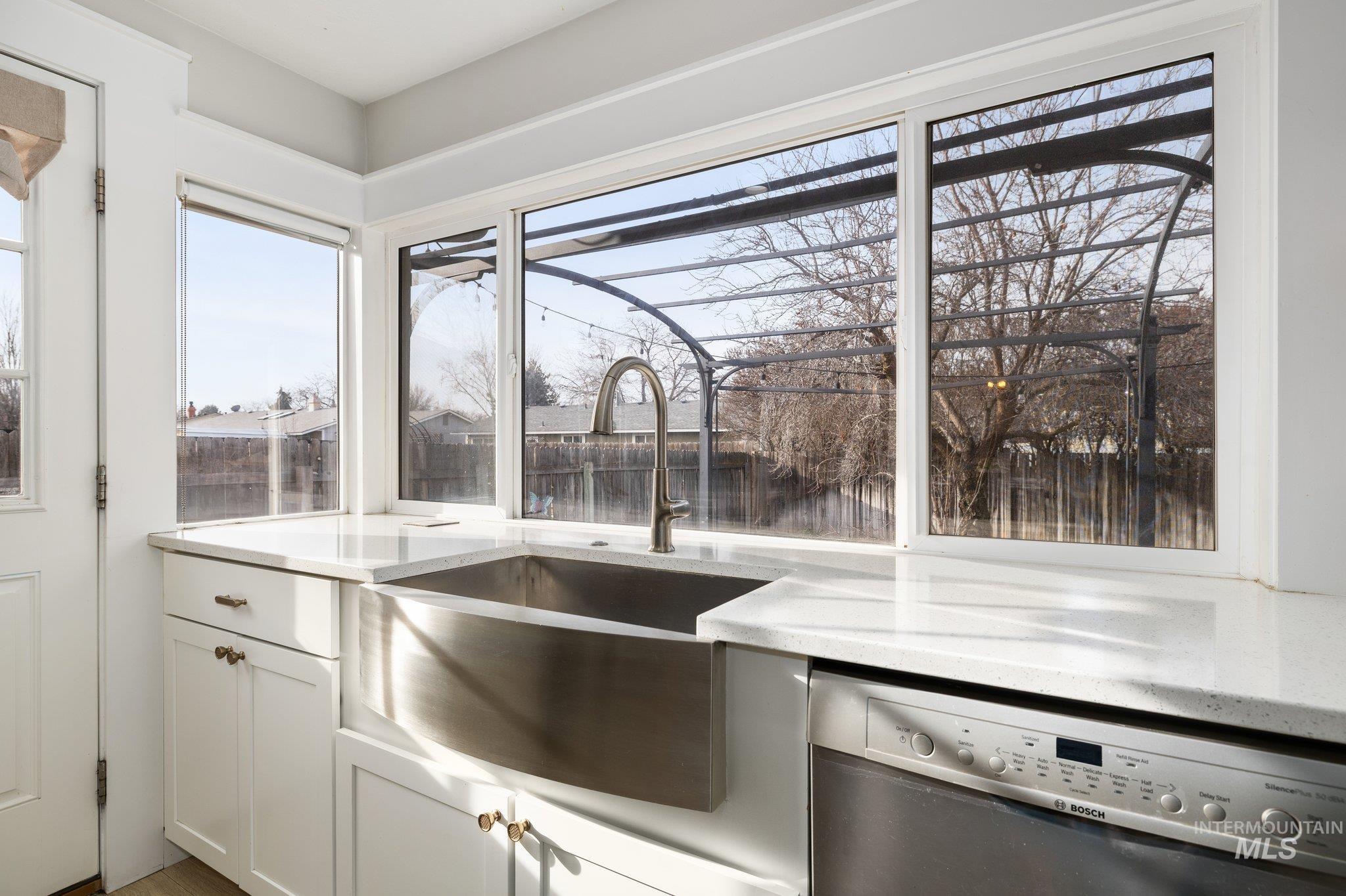Kitchen with stainless steel dishwasher, white cabinetry, and light stone counters