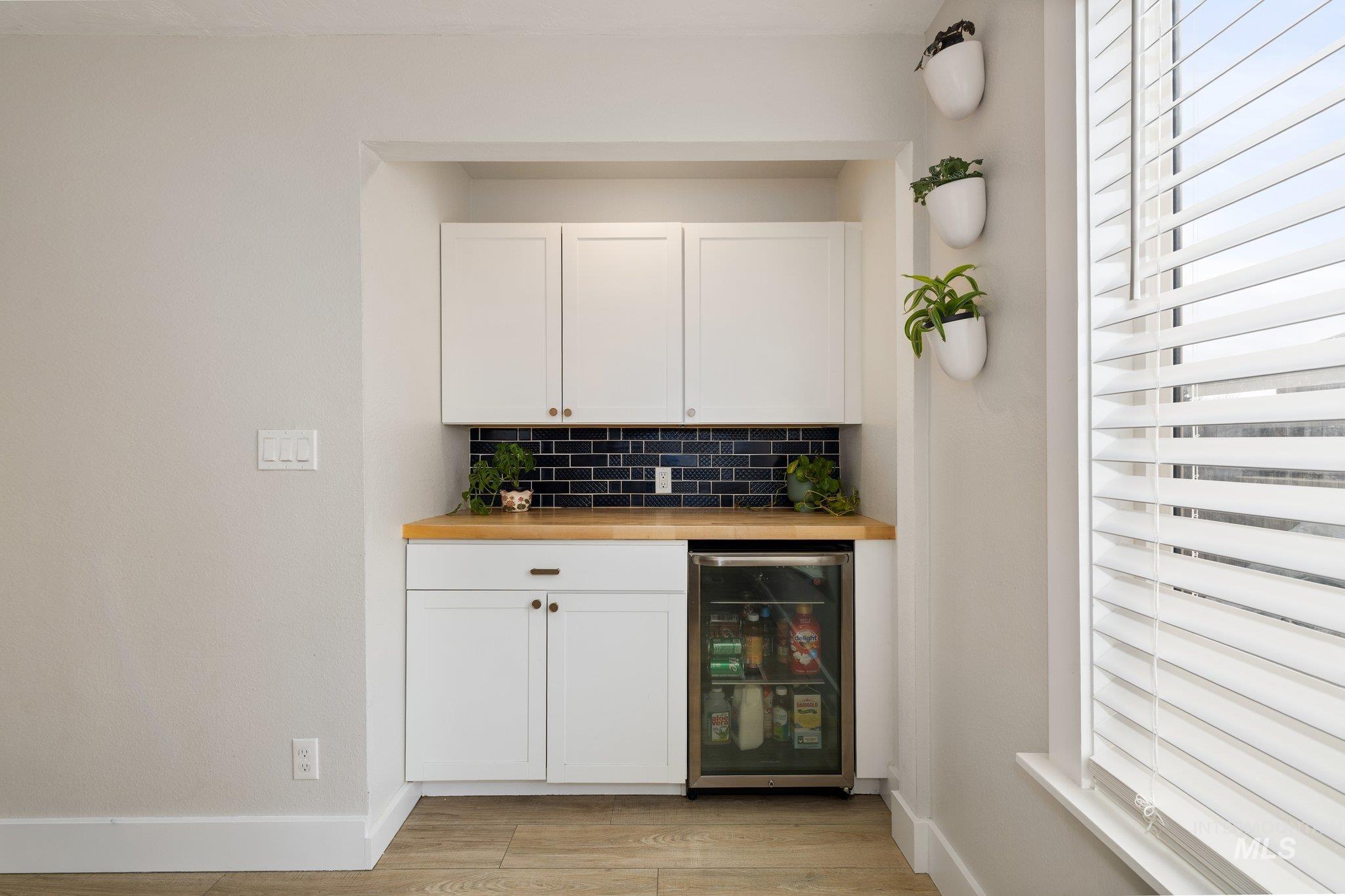 Indoor dry bar with white cabinets, backsplash, beverage cooler, and plenty of natural light