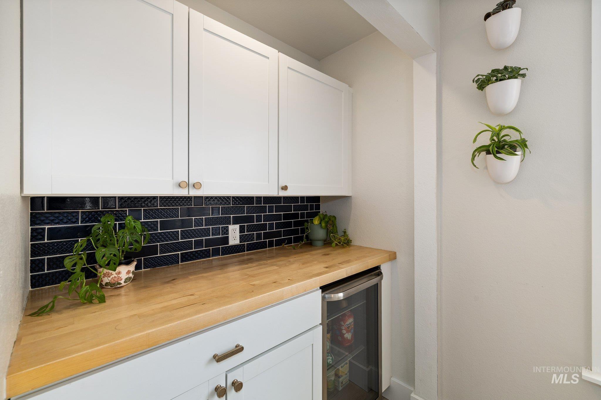 Bar area with wood counters, white cabinets, wine cooler, and tasteful backsplash