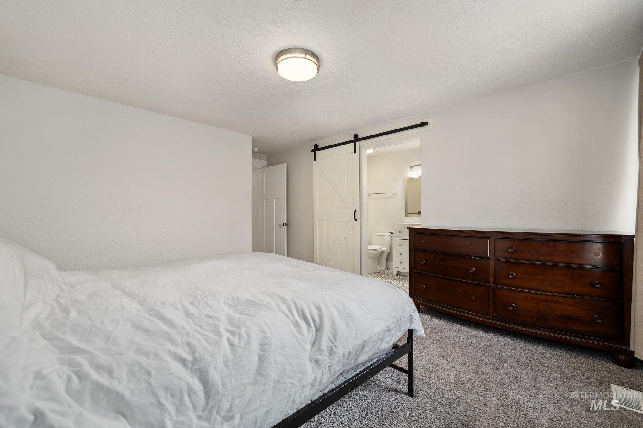 Bedroom featuring a barn door, light carpet, ensuite bathroom, and a textured ceiling