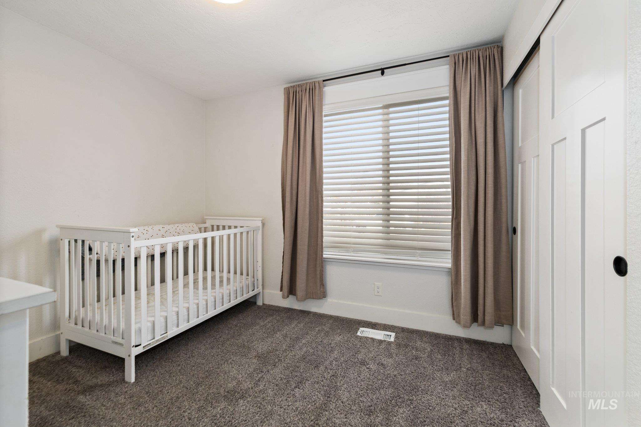 Bedroom featuring a nursery area, dark carpet, and a closet