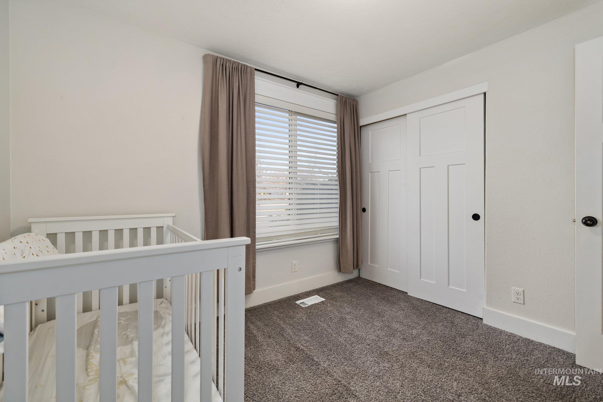 Unfurnished bedroom featuring dark colored carpet, a closet, and a crib