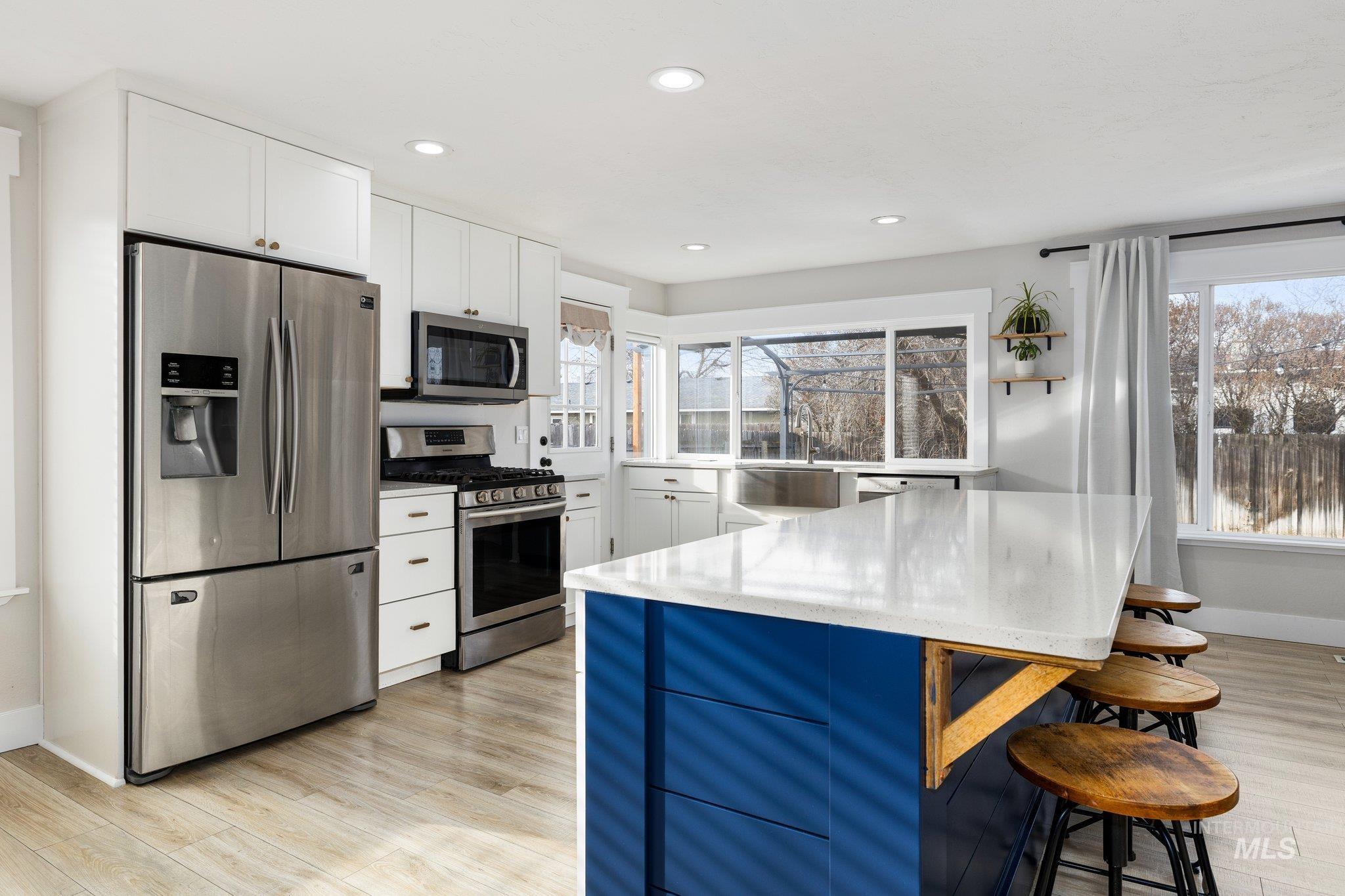 Kitchen with white cabinetry, appliances with stainless steel finishes, a breakfast bar, blue cabinetry, and light wood-style floors