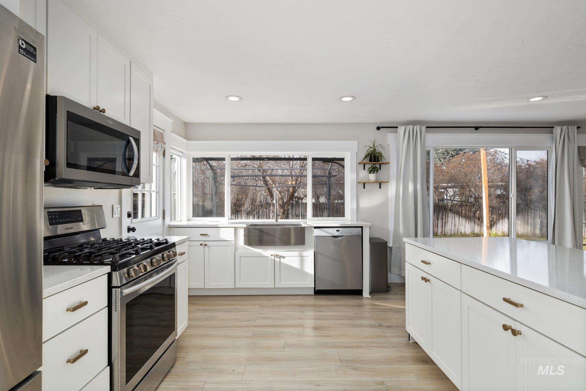 Kitchen with appliances with stainless steel finishes, white cabinets, light wood-type flooring, recessed lighting, and light stone counters