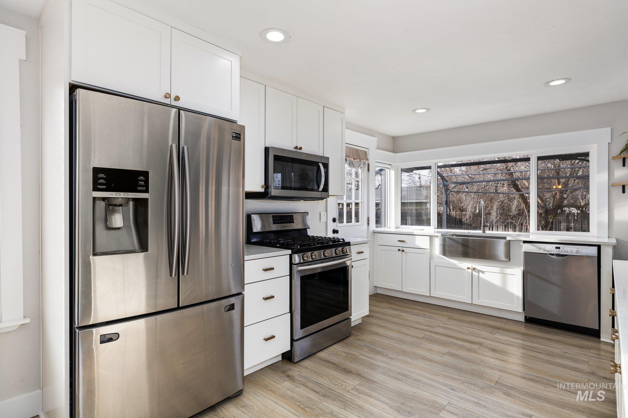 Kitchen with stainless steel appliances, white cabinetry, light countertops, light wood-style floors, and recessed lighting