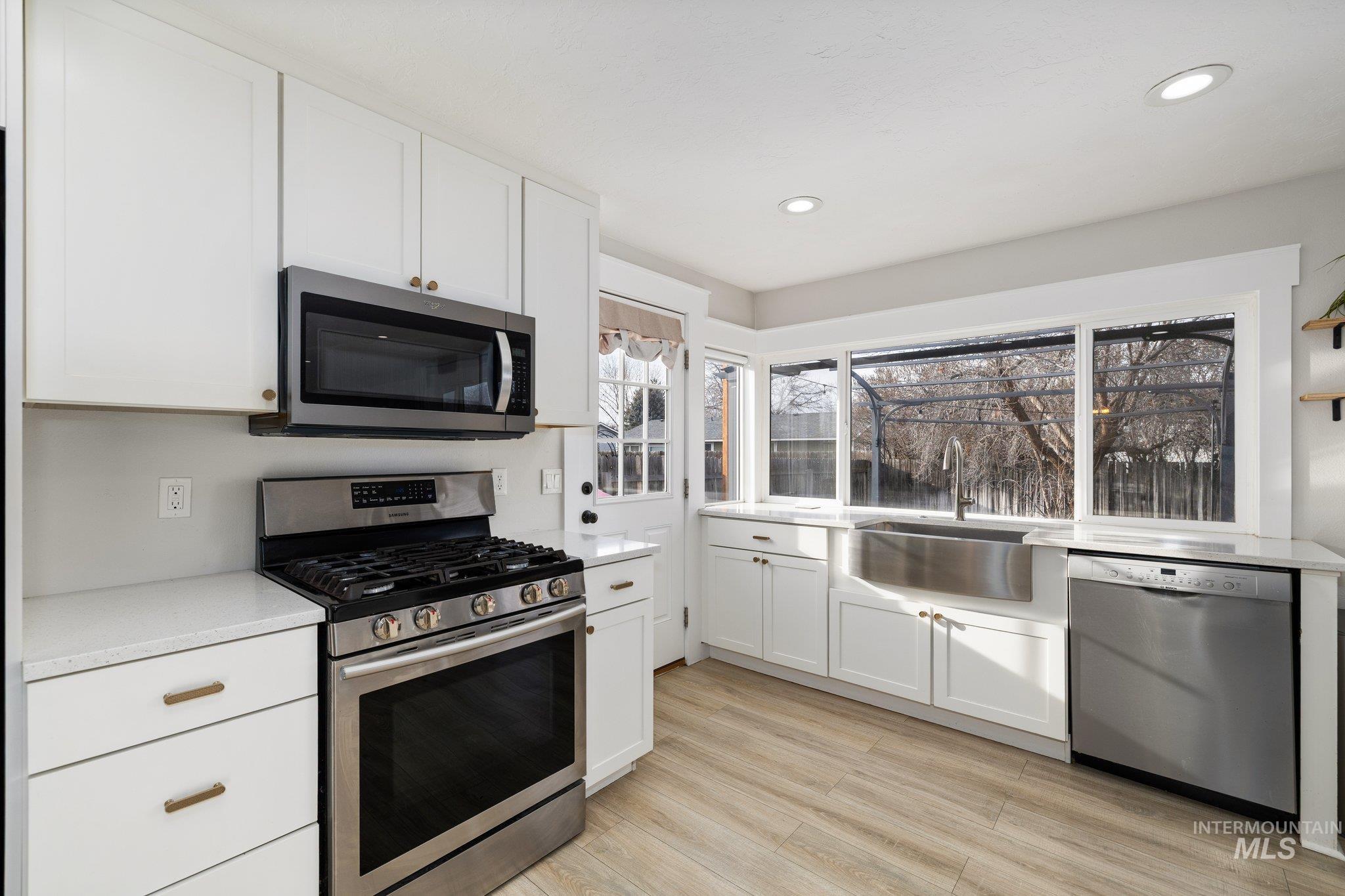 Kitchen with stainless steel appliances, white cabinets, light wood-style flooring, light stone countertops, and recessed lighting
