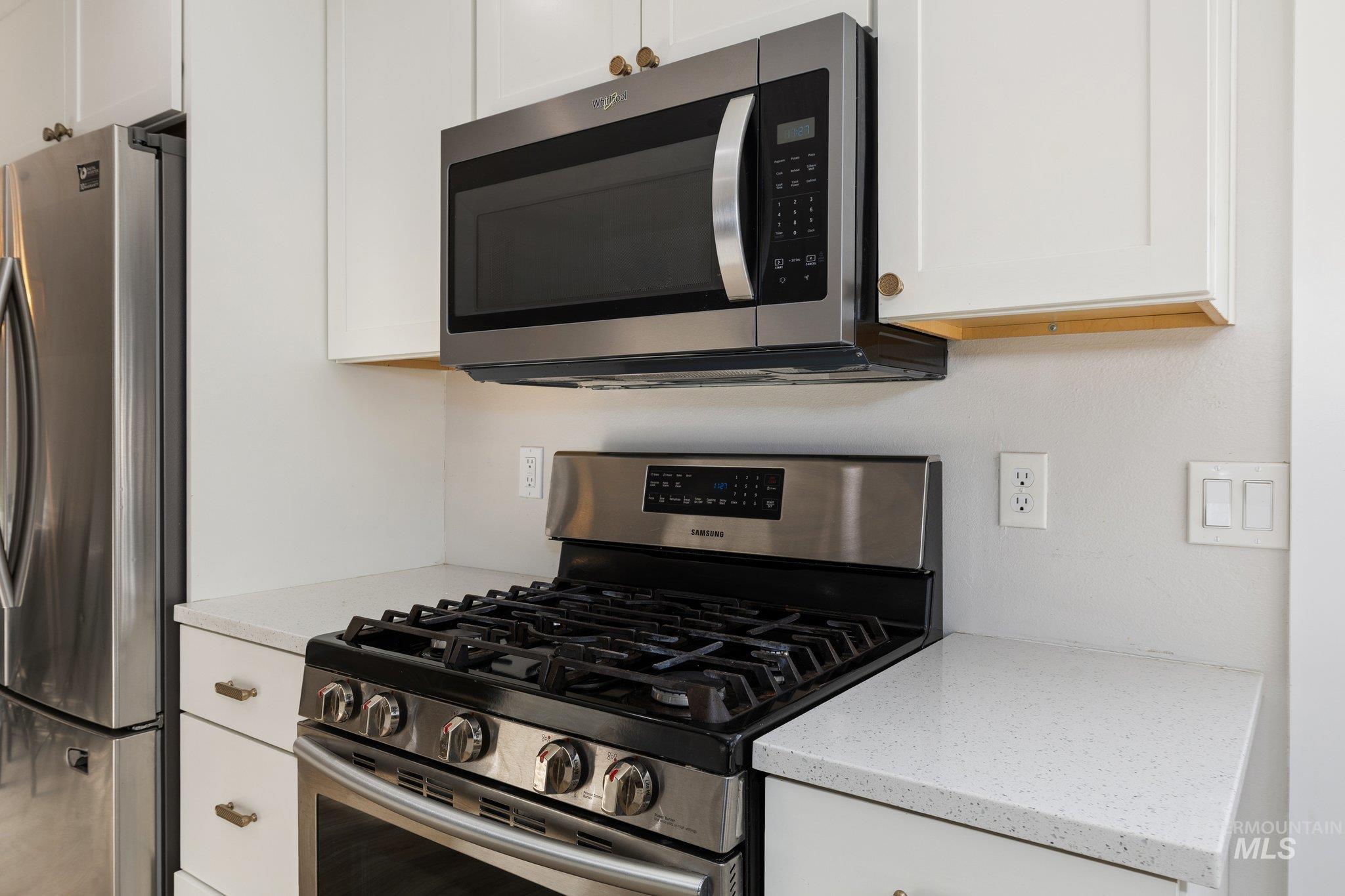 Kitchen featuring stainless steel appliances, white cabinets, and light stone counters