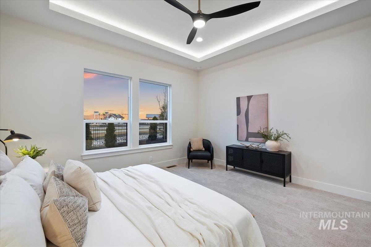 Bedroom with light carpet, ceiling fan, and a raised ceiling