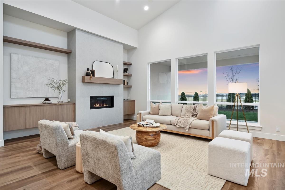 Living room with a towering ceiling, light wood-style flooring, and a glass covered fireplace