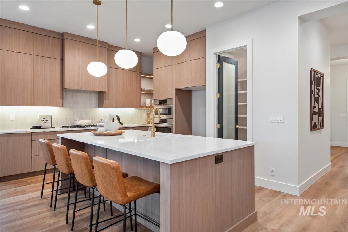Kitchen featuring modern cabinets, backsplash, a kitchen breakfast bar, light wood-style floors, and recessed lighting