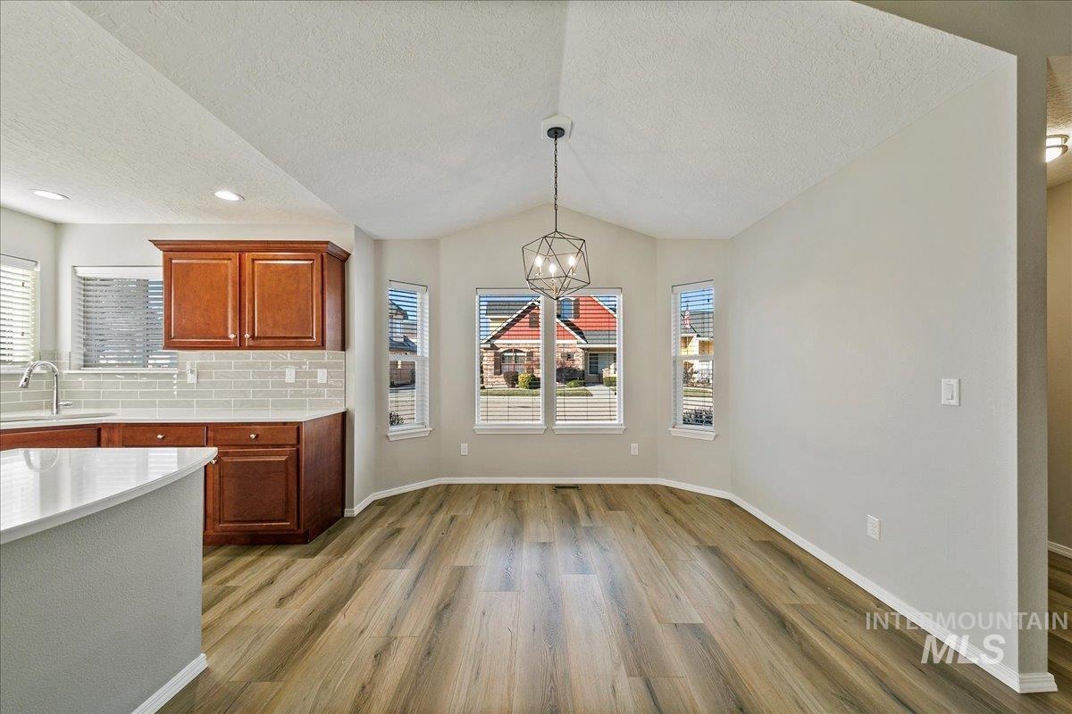 Kitchen with backsplash, a textured ceiling, light wood-type flooring, a chandelier, and decorative light fixtures