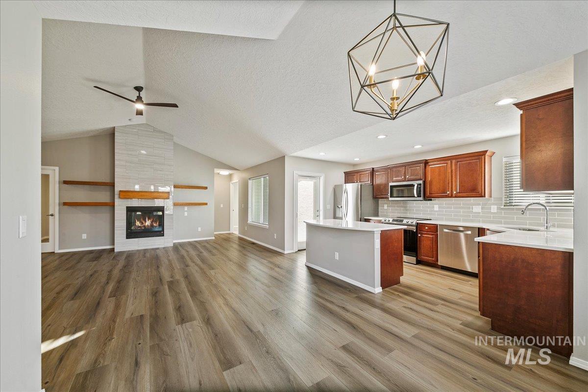 Kitchen with open floor plan, a fireplace, stainless steel appliances, vaulted ceiling, and a kitchen island