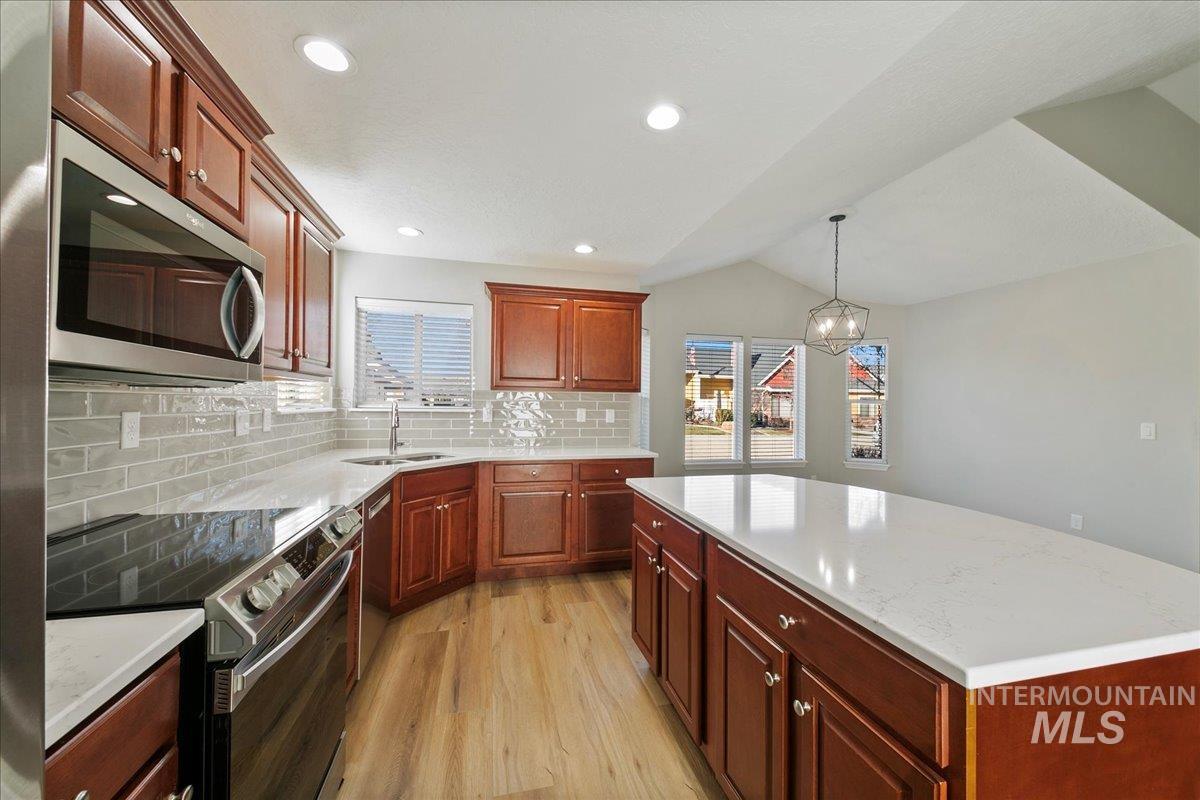 Kitchen with stainless steel appliances, a center island, backsplash, hanging light fixtures, and light wood-type flooring