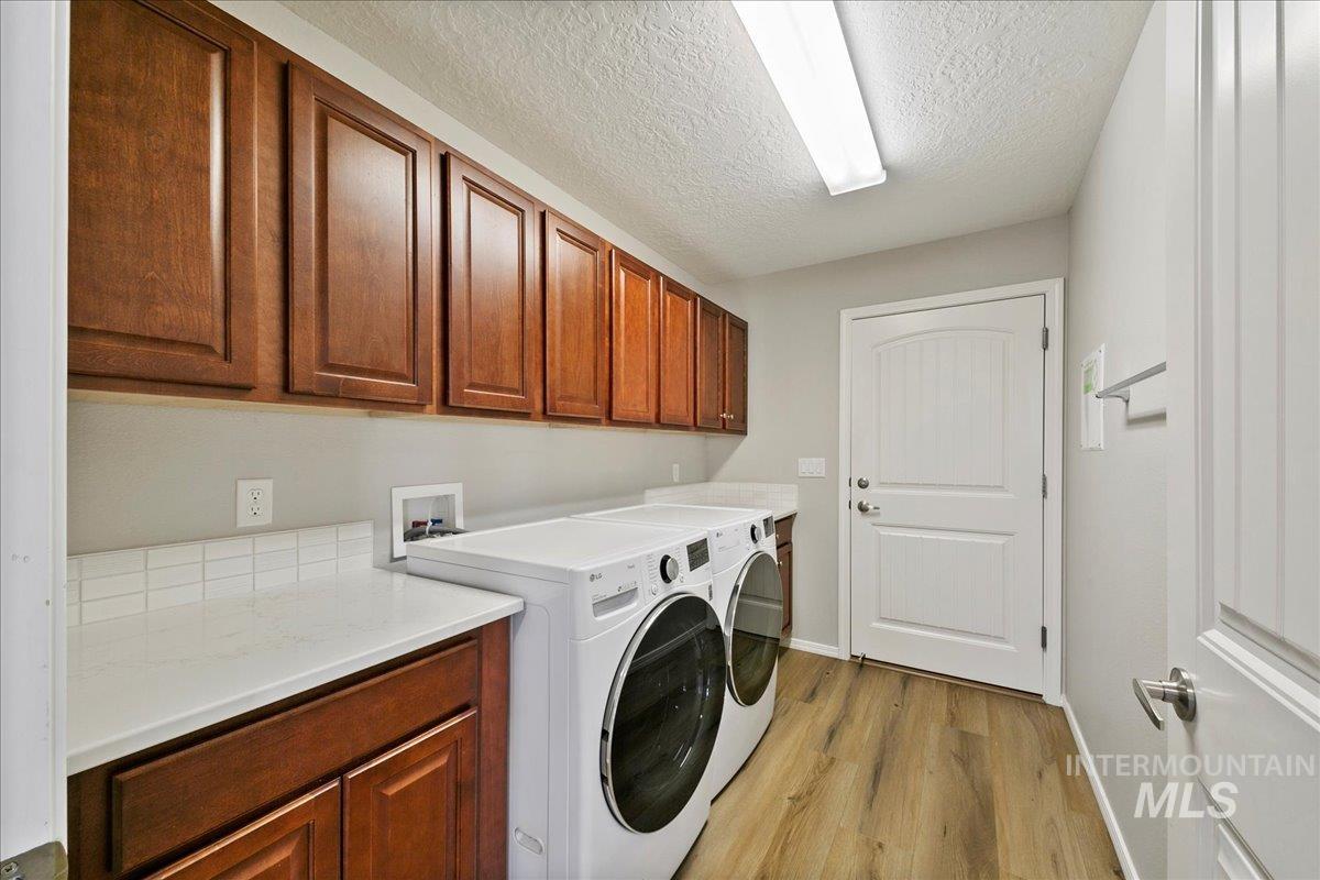 Laundry area with washer and dryer, a textured ceiling, light wood-type flooring, and cabinet space