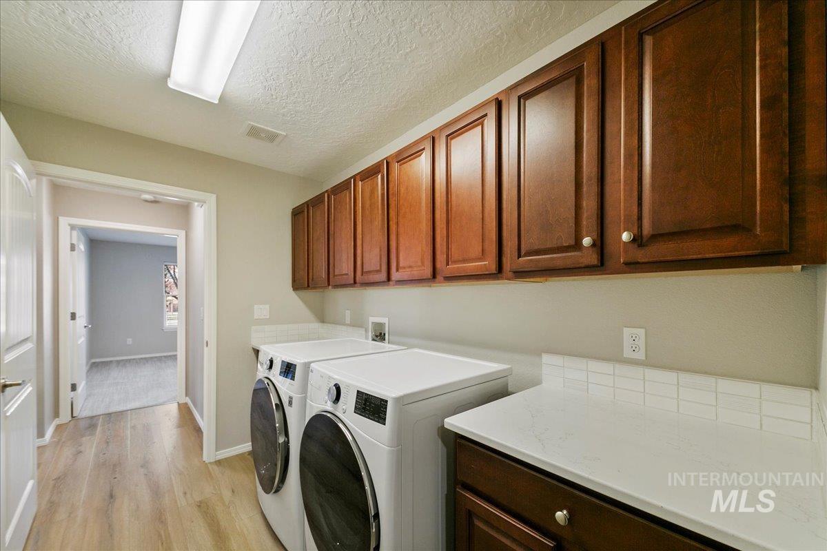 Washroom with a textured ceiling, light wood-type flooring, washing machine and dryer, and cabinet space