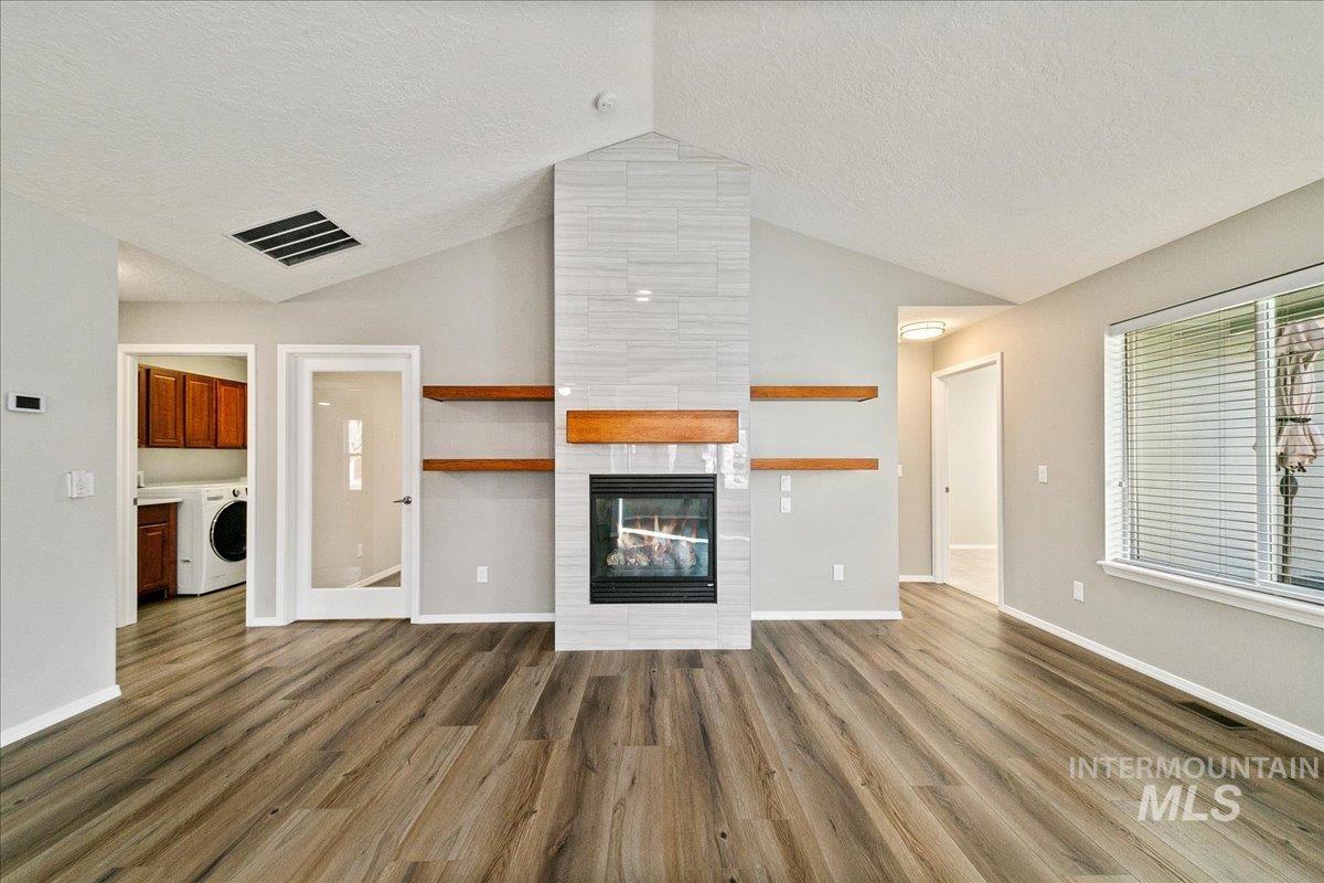Unfurnished living room with vaulted ceiling, a tiled fireplace, a textured ceiling, dark wood-type flooring, and washer / dryer