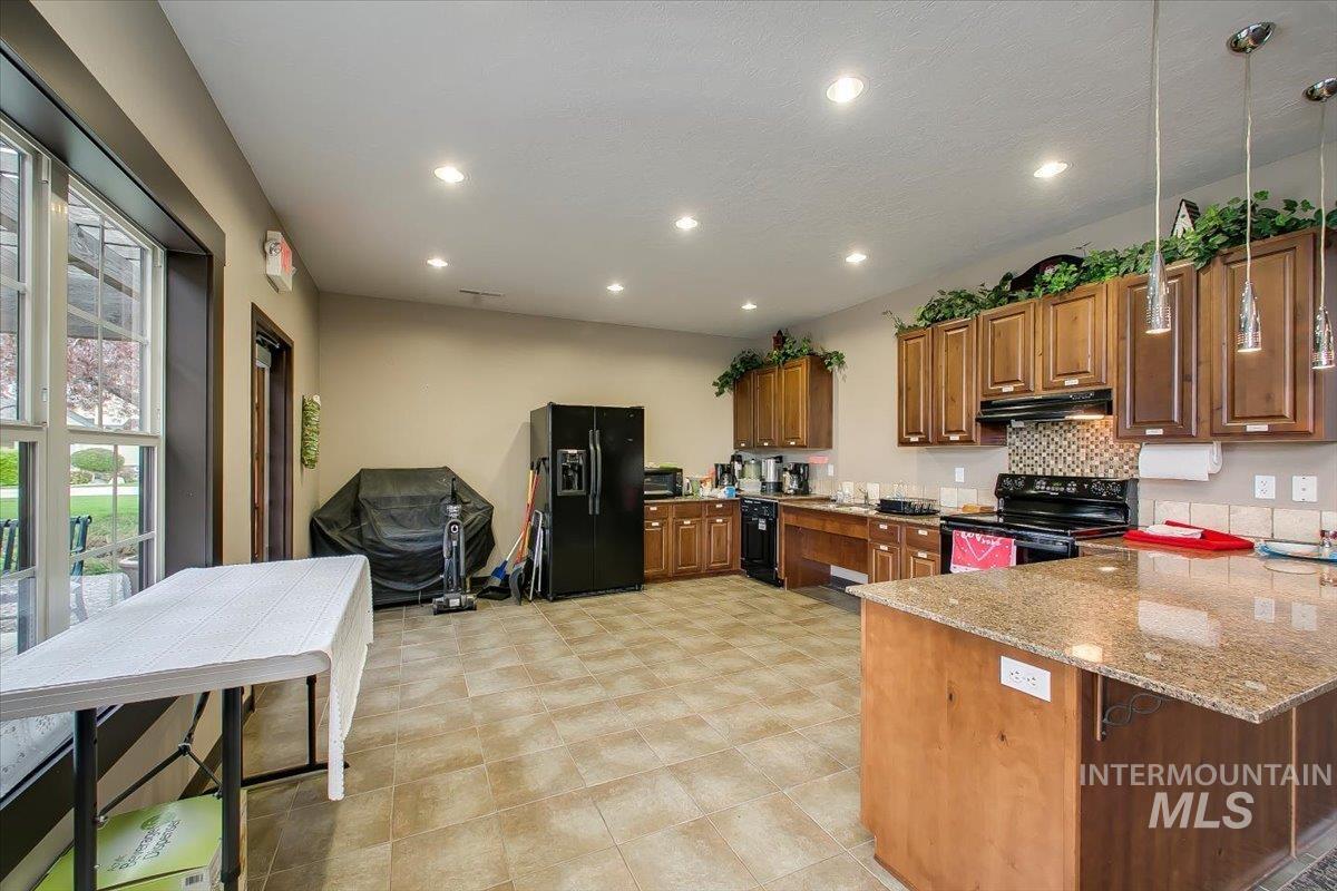 Kitchen with brown cabinets, a peninsula, black appliances, a kitchen breakfast bar, and light stone countertops