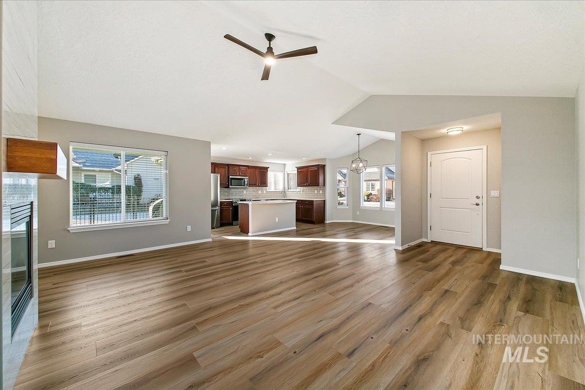 Unfurnished living room featuring dark wood-style floors, ceiling fan, vaulted ceiling, a chandelier, and a fireplace