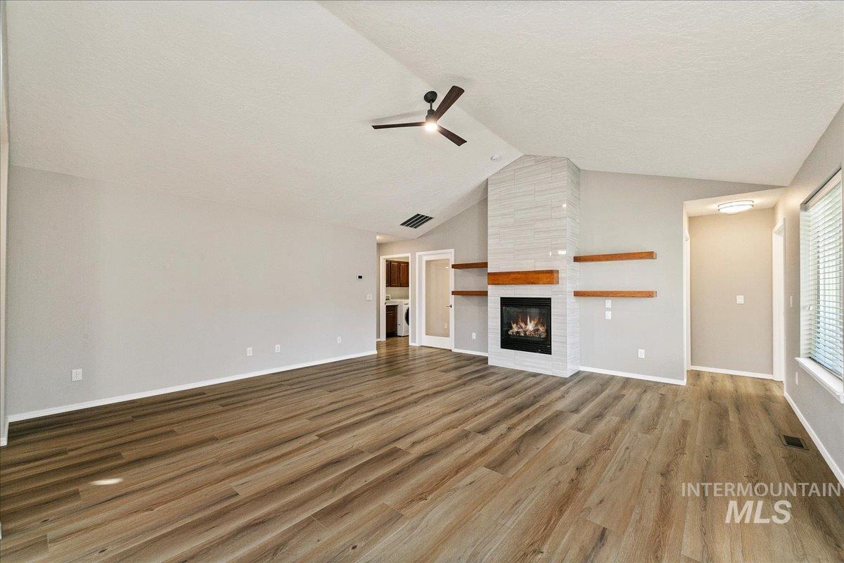 Unfurnished living room with a fireplace, vaulted ceiling, wood finished floors, a textured ceiling, and ceiling fan