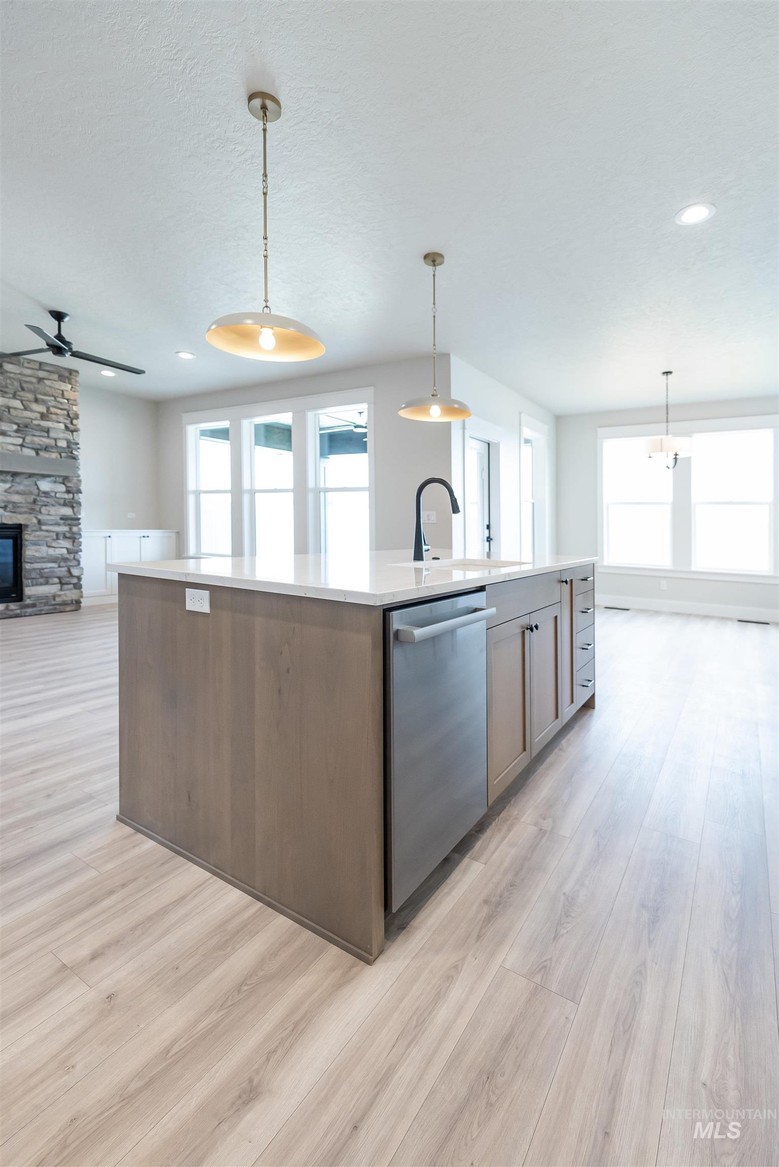 Kitchen with open floor plan, decorative light fixtures, a kitchen island with sink, dishwasher, and a fireplace