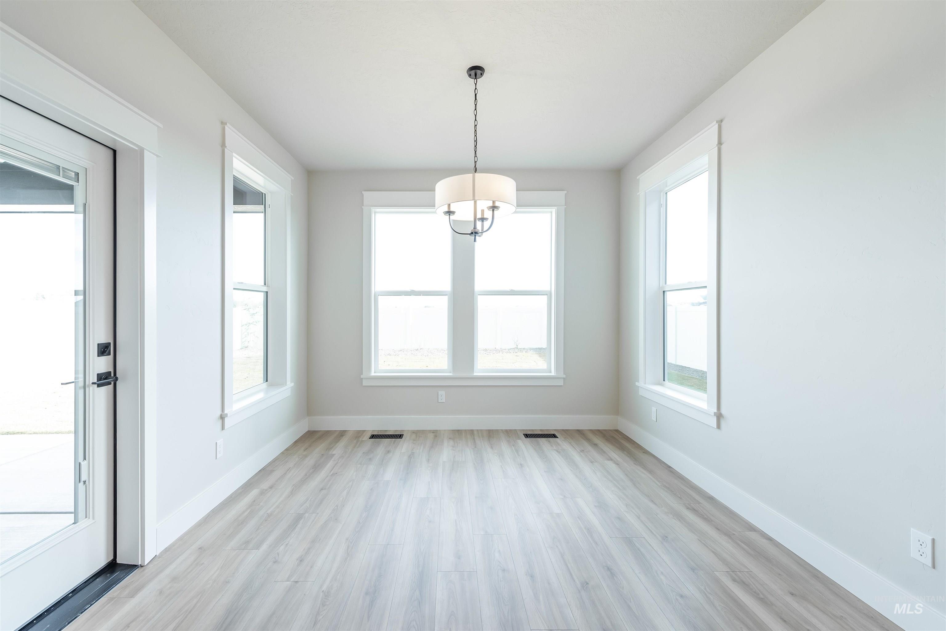 Unfurnished dining area with light wood finished floors, plenty of natural light, and a chandelier