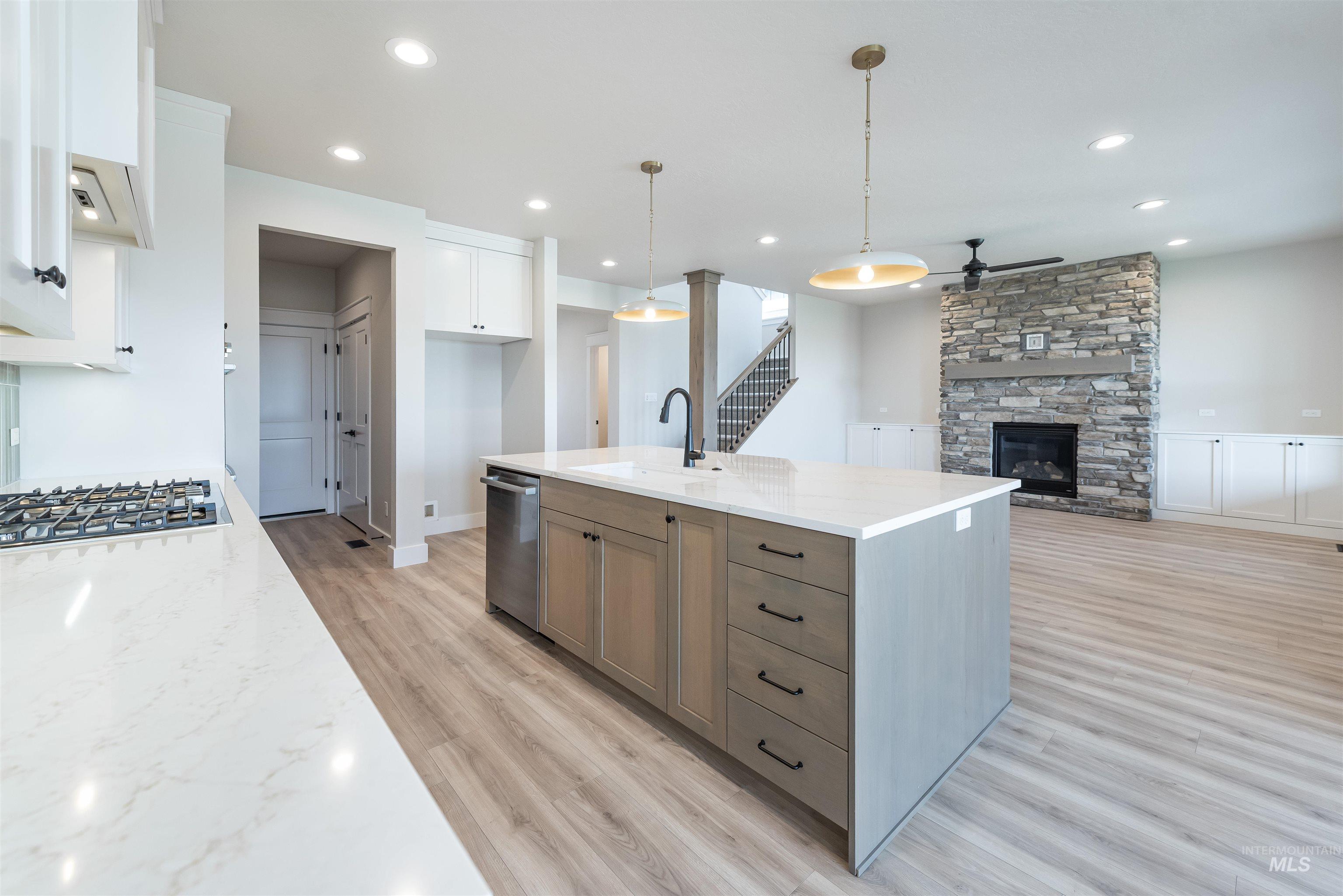 Kitchen with light stone countertops, an island with sink, a ceiling fan, open floor plan, and pendant lighting