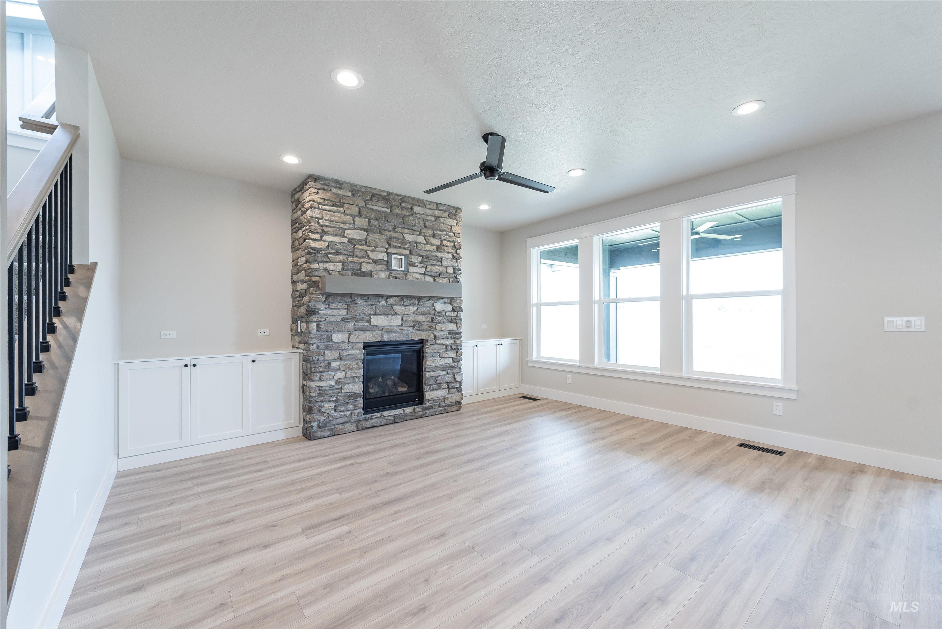 Unfurnished living room featuring a ceiling fan, a fireplace, light wood-style flooring, stairs, and recessed lighting