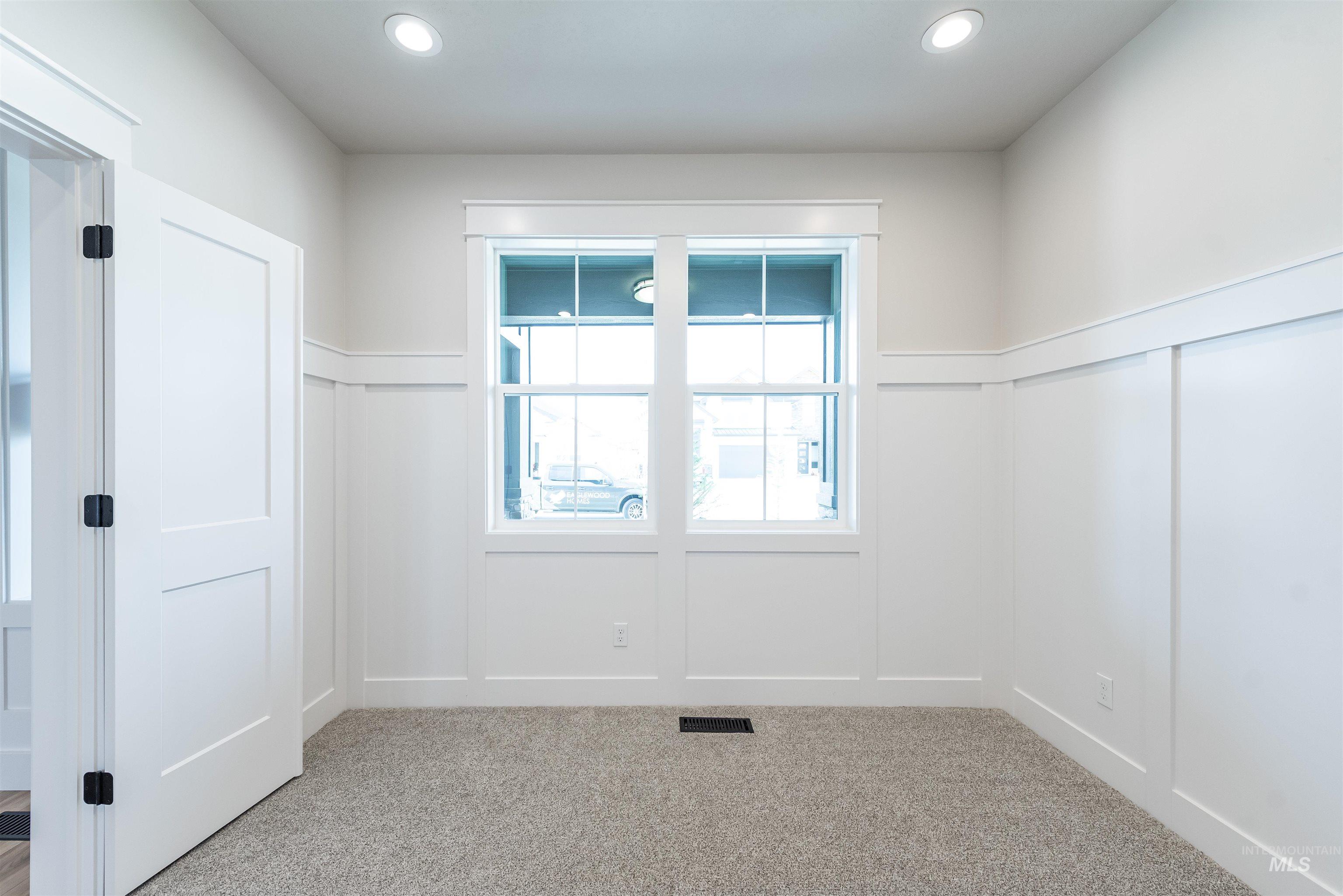 Empty room featuring a decorative wall, carpet floors, wainscoting, and recessed lighting
