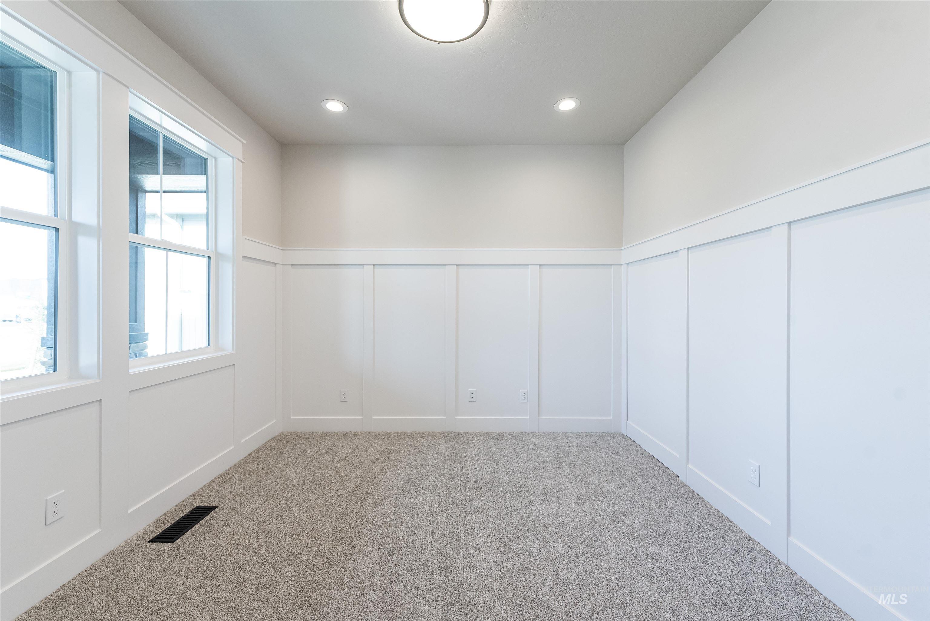 Empty room with a decorative wall, wainscoting, light carpet, and recessed lighting