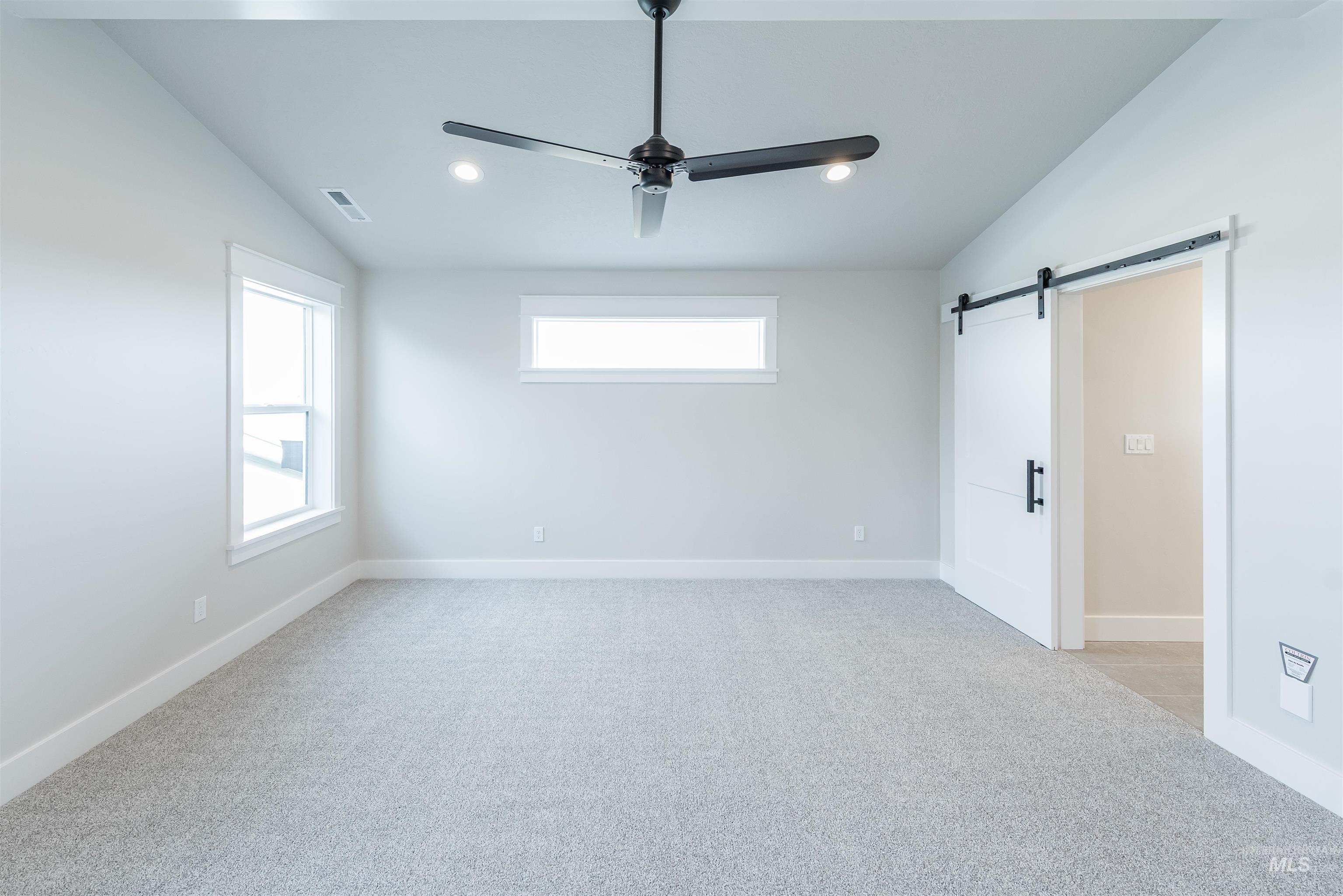 Empty room featuring a barn door, vaulted ceiling, plenty of natural light, light colored carpet, and a ceiling fan