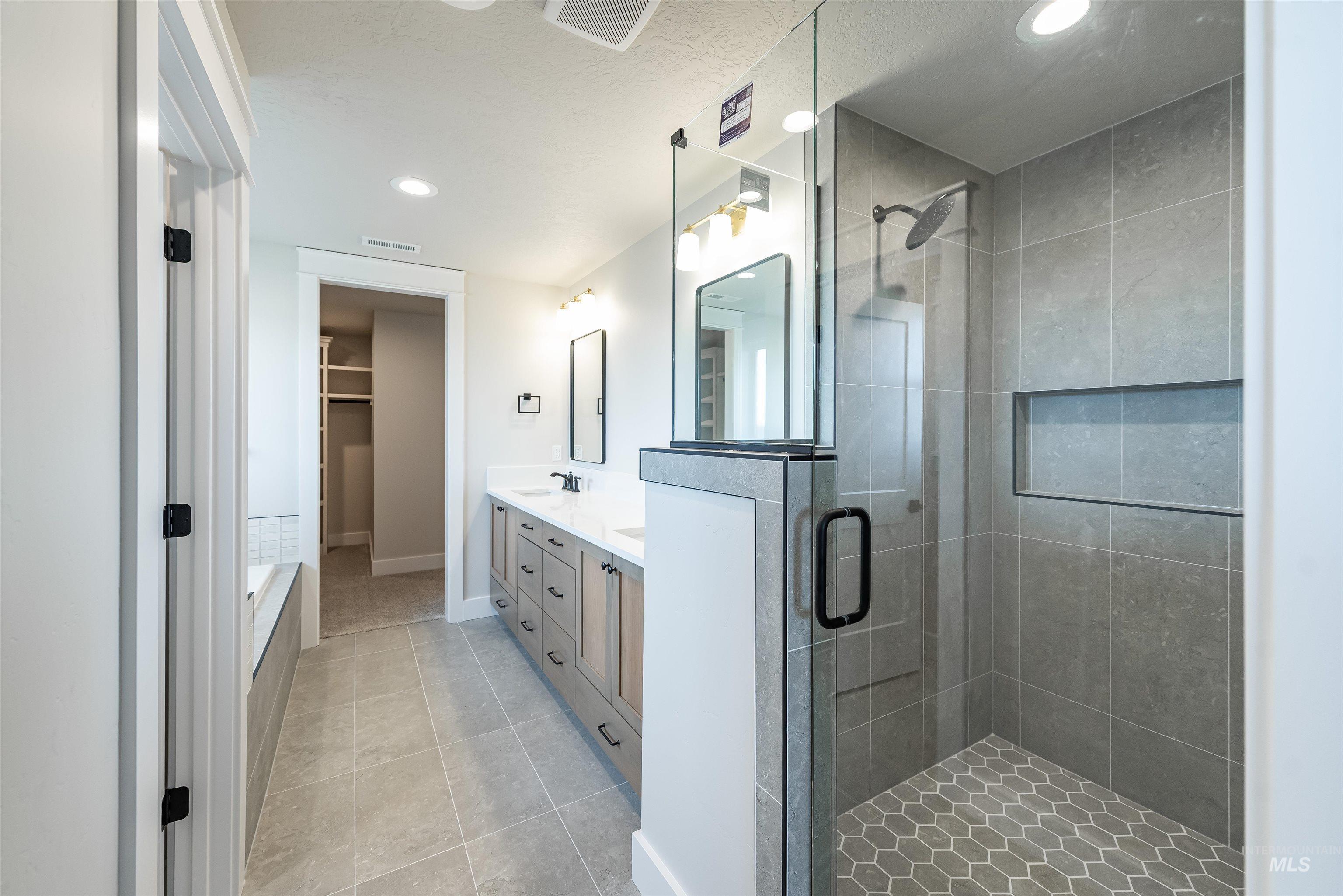 Full bath featuring a spacious closet, double vanity, a shower stall, recessed lighting, and light tile patterned floors