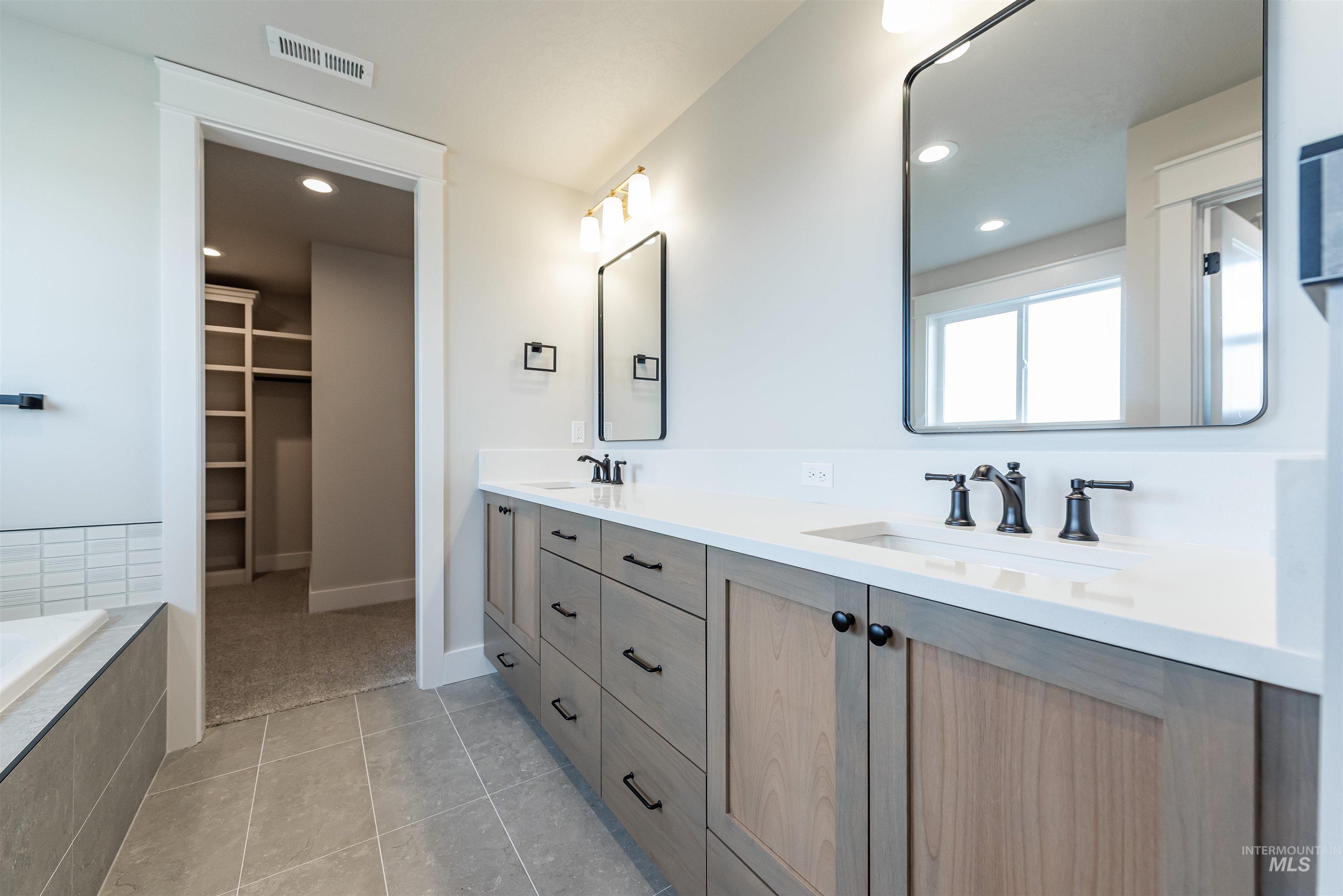 Bathroom featuring double vanity, light tile patterned floors, recessed lighting, a walk in closet, and a relaxing tiled tub