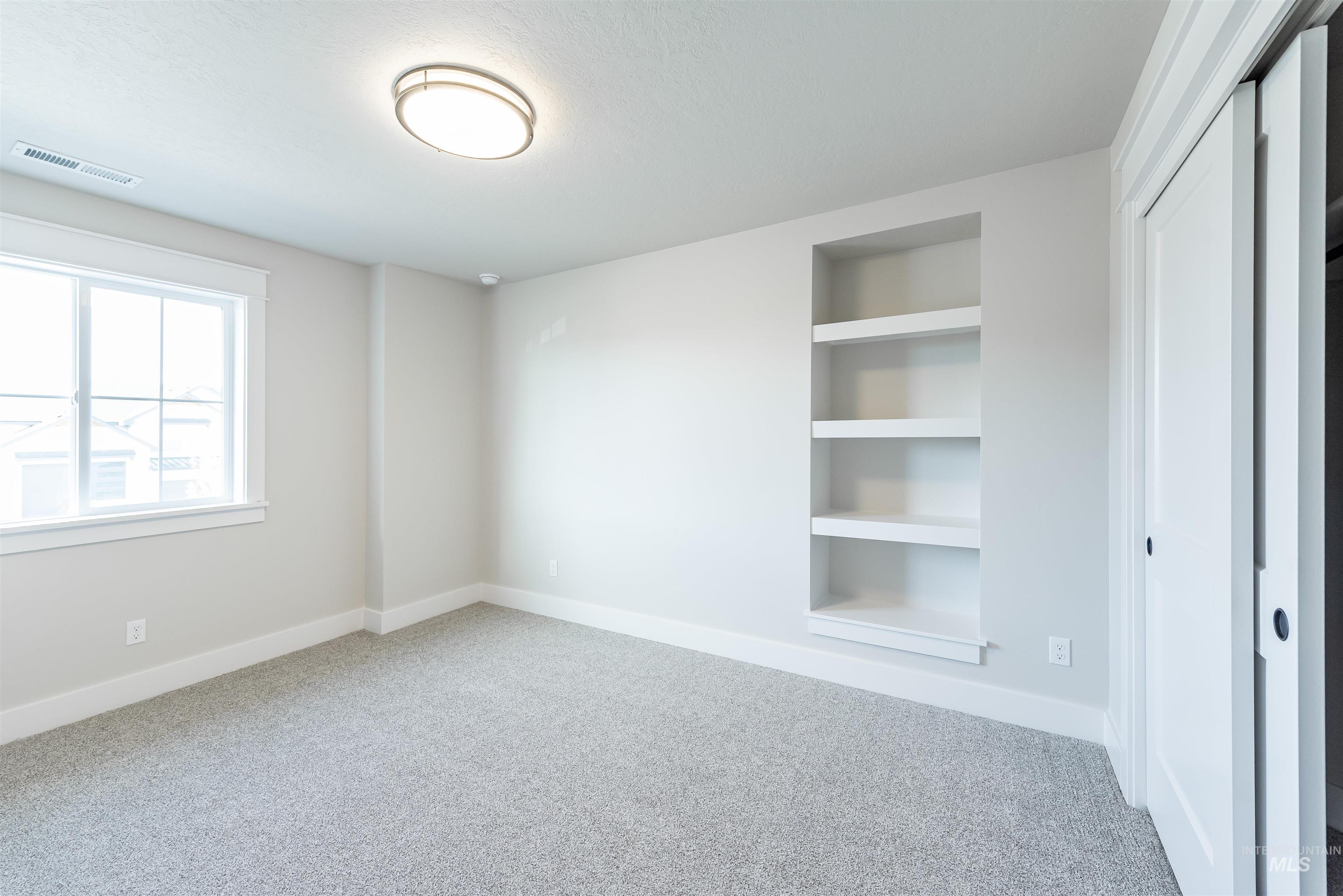 Unfurnished room with built in shelves and light colored carpet